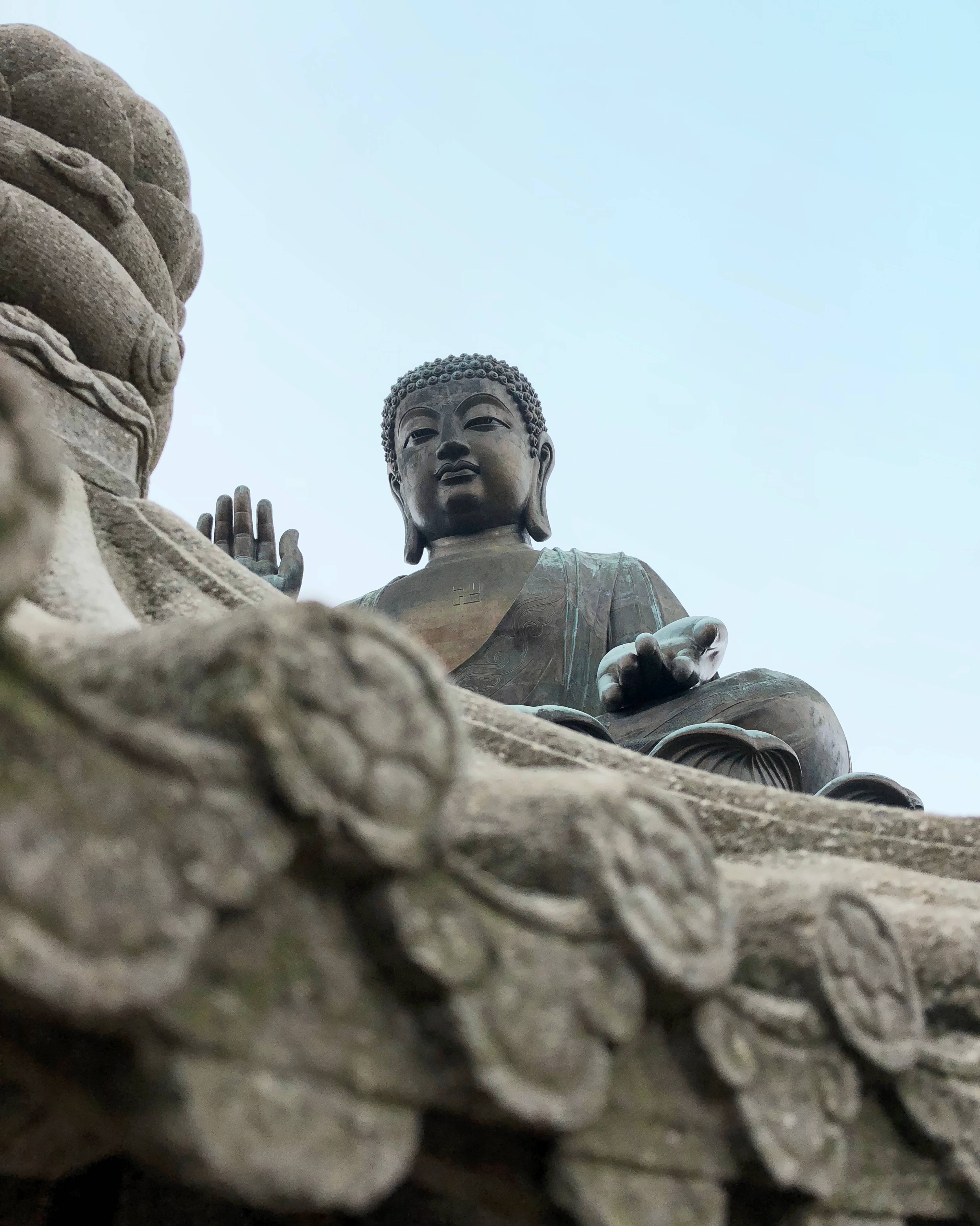 Gautam Buddha 桌布 壁紙 — 低角度拍攝捕捉到一座寧靜的青銅佛像，坐落在華麗的石造建築上，以蒼白的天空為背景。