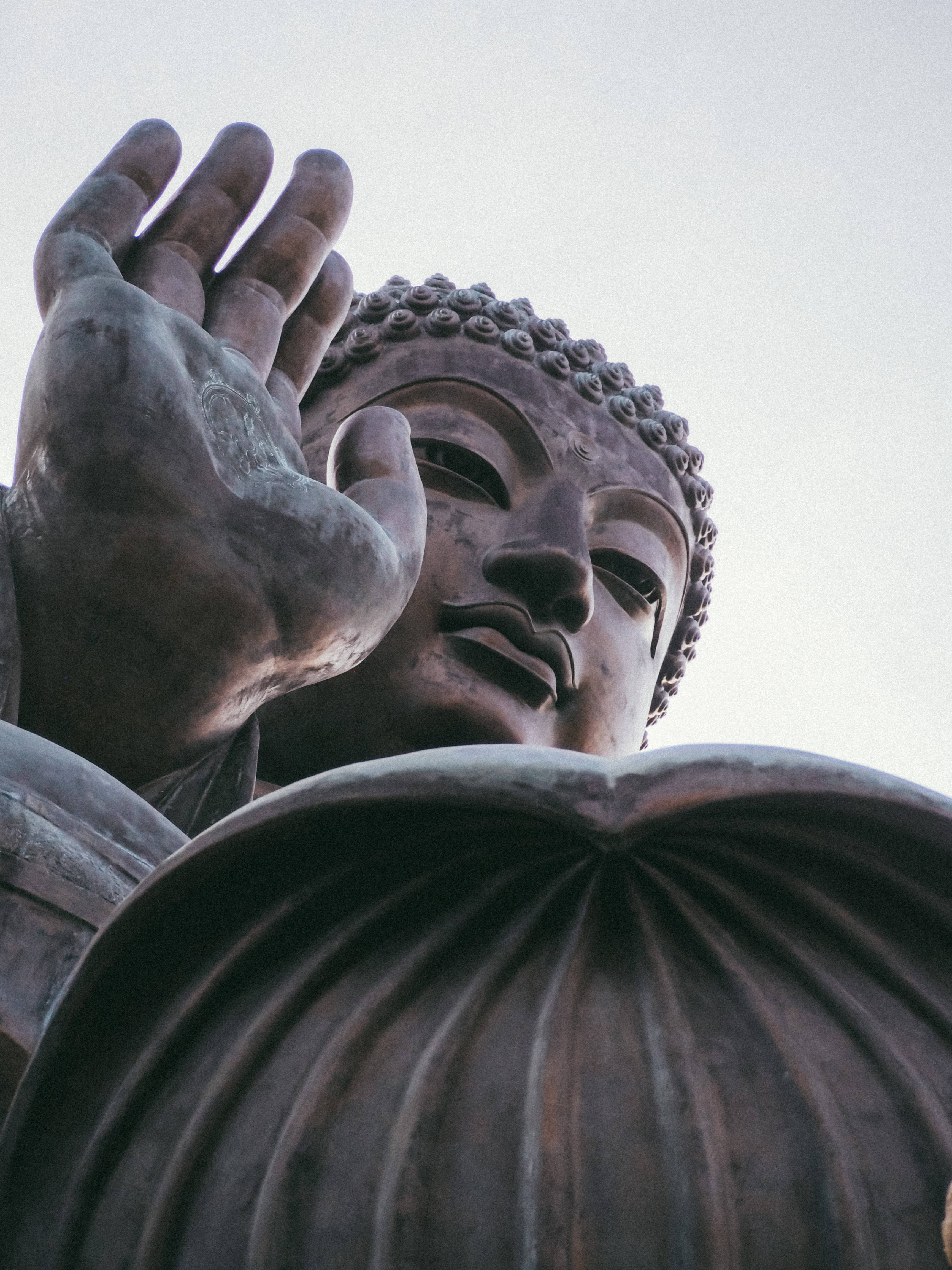 Gautam Buddha 桌布 壁紙 — 低角度拍攝捕捉到一座巨大青銅佛像寧靜的面容和舉起的手，背景是蒼白的天空。