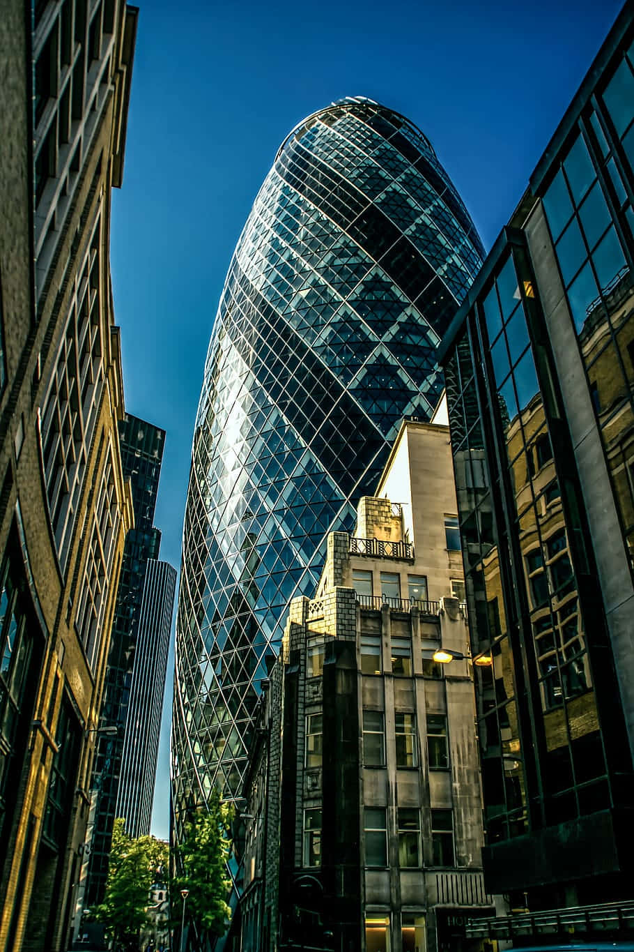 Skyscraper 桌布 壁紙 — 低角度拍攝捕捉到標誌性的小黃瓜摩天大樓刺穿清澈的藍天，兩旁是較舊的磚砌建築。