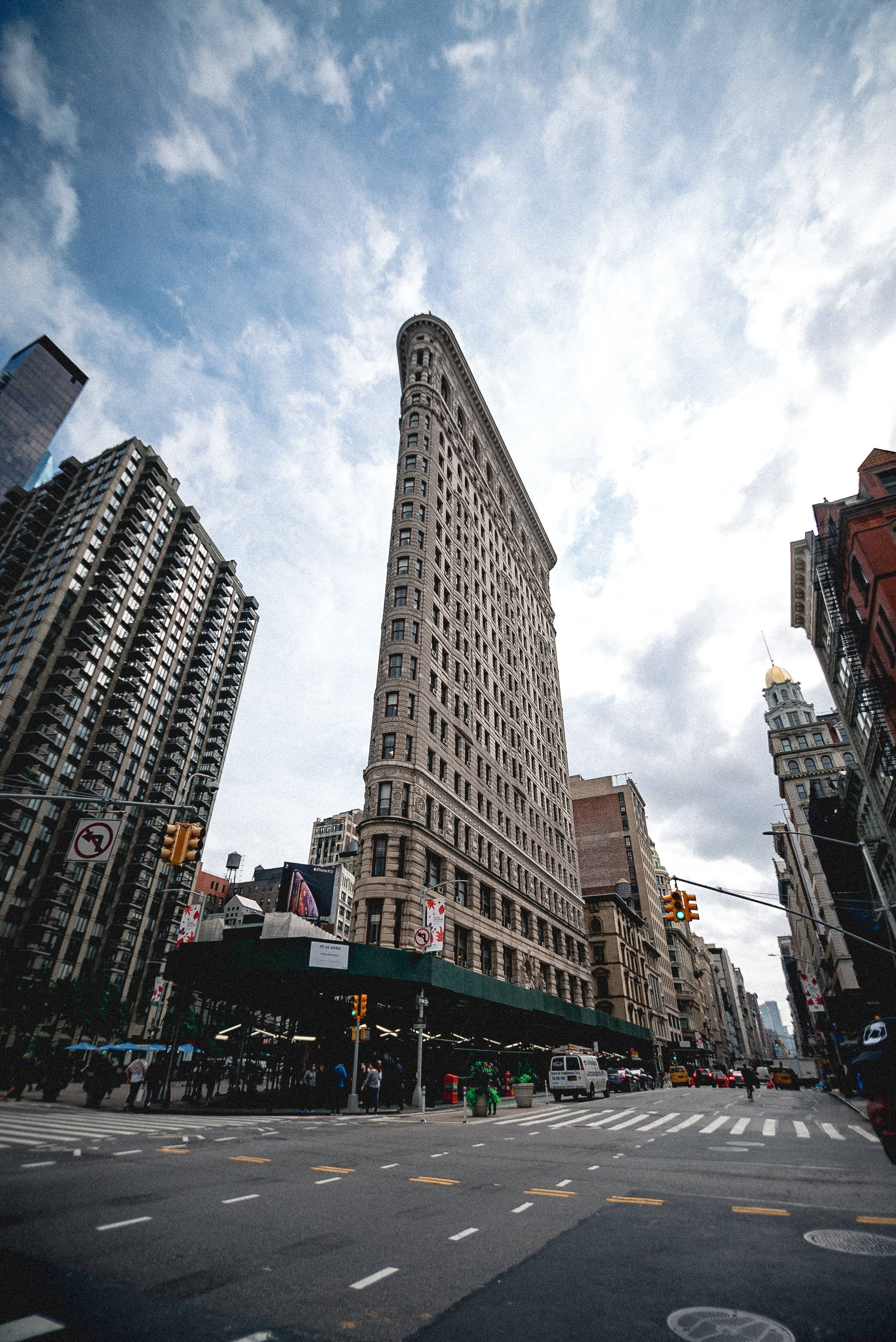 Flatiron Building 桌布 壁紙 — 低角度拍攝捕捉到標誌性的熨斗大廈在紐約市繁忙的街道場景中刺穿部分多雲的天空。