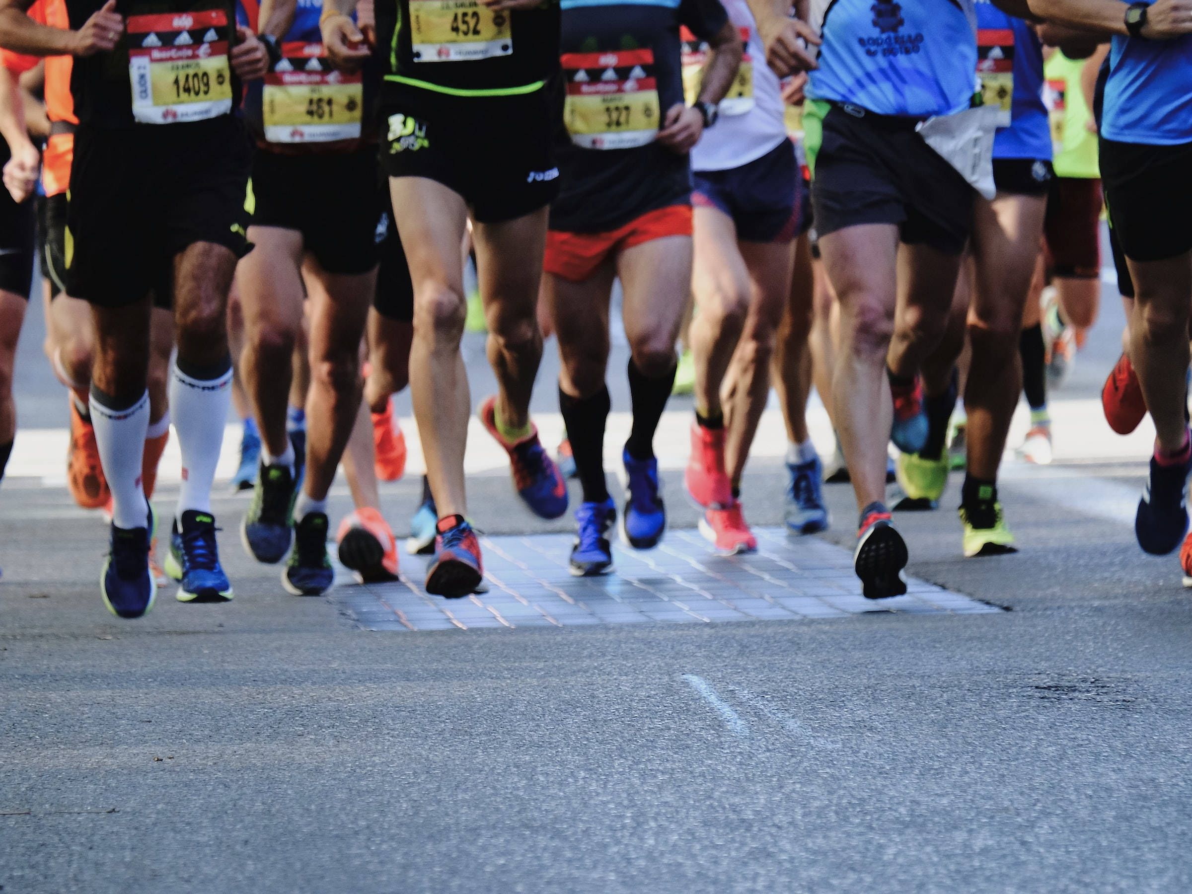 Athletic 桌布 壁紙 — 低角度拍攝捕捉到眾多馬拉松跑者在鋪砌街道上移動的雙腿和跑鞋。