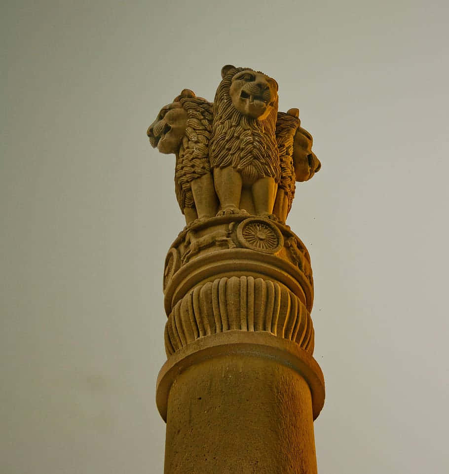 statue 桌布 壁紙 — 低角度拍攝捕捉到風化的石造阿育王柱，頂部有四隻雕刻精細的獅子，襯著蒼白的天空。