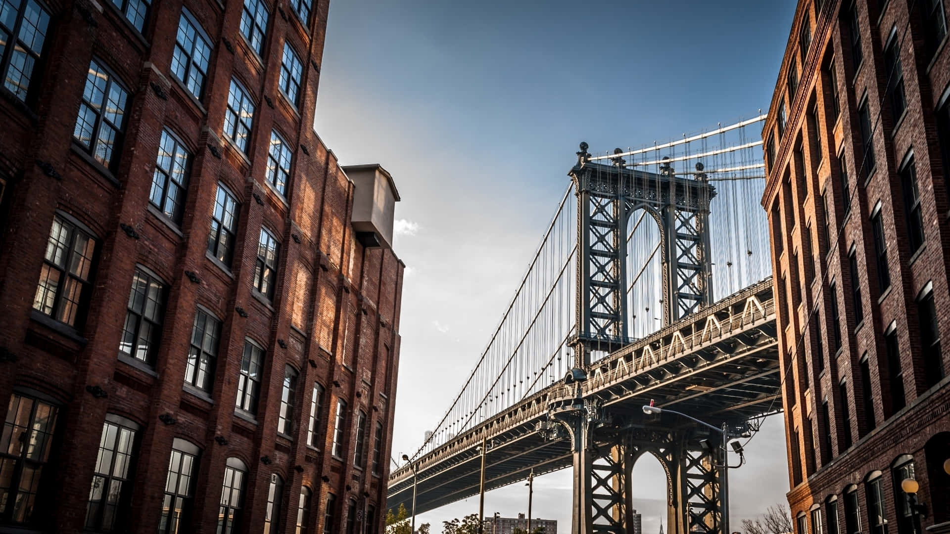 Nyc 桌布 壁紙 — 低角度拍攝曼哈頓大橋，被高聳的紅磚建築環繞，背景是清澈的藍天。