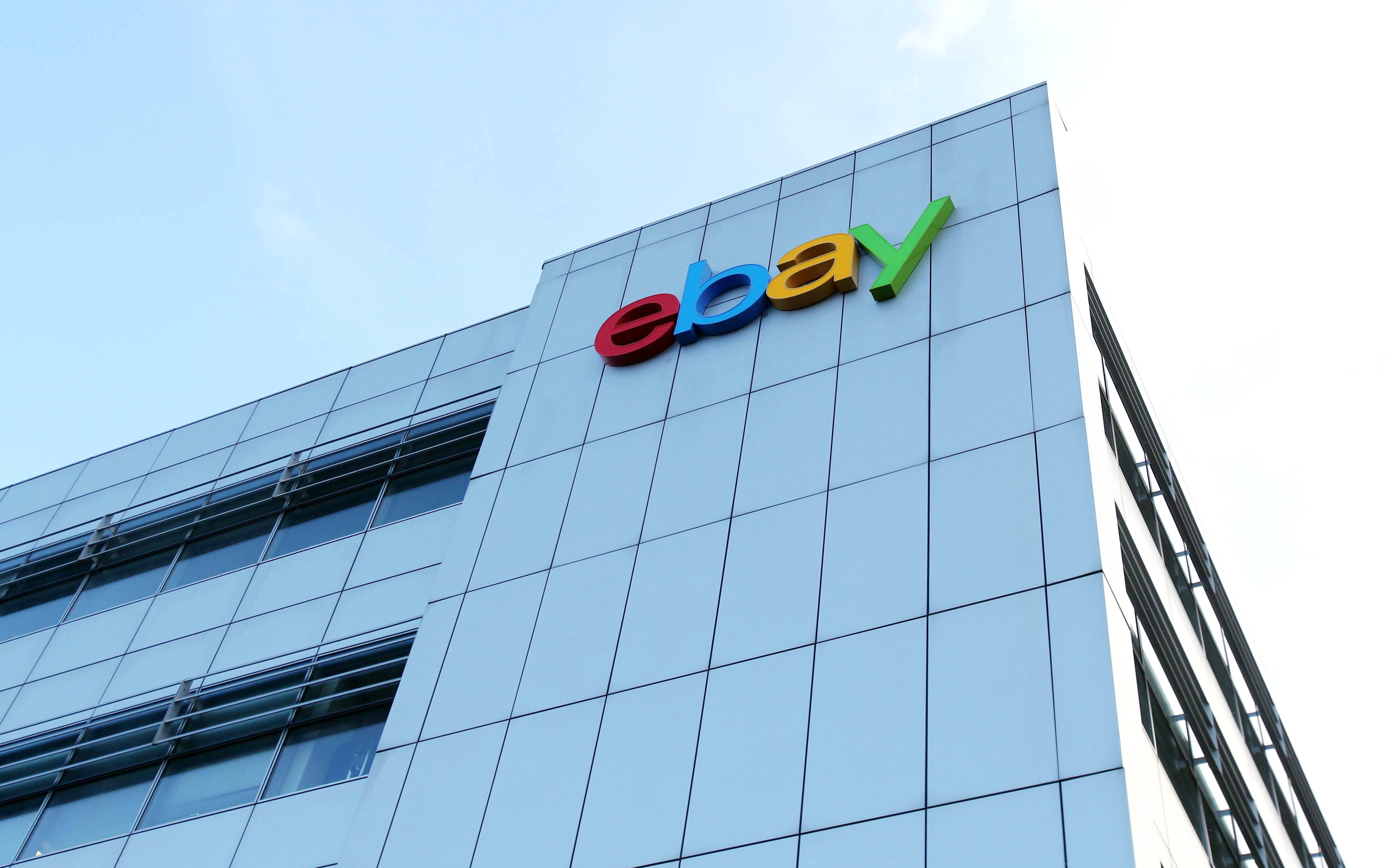 eBay 桌布 壁紙 — 低角度拍攝現代玻璃建築，色彩繽紛的eBay標誌映襯著清澈的藍天。