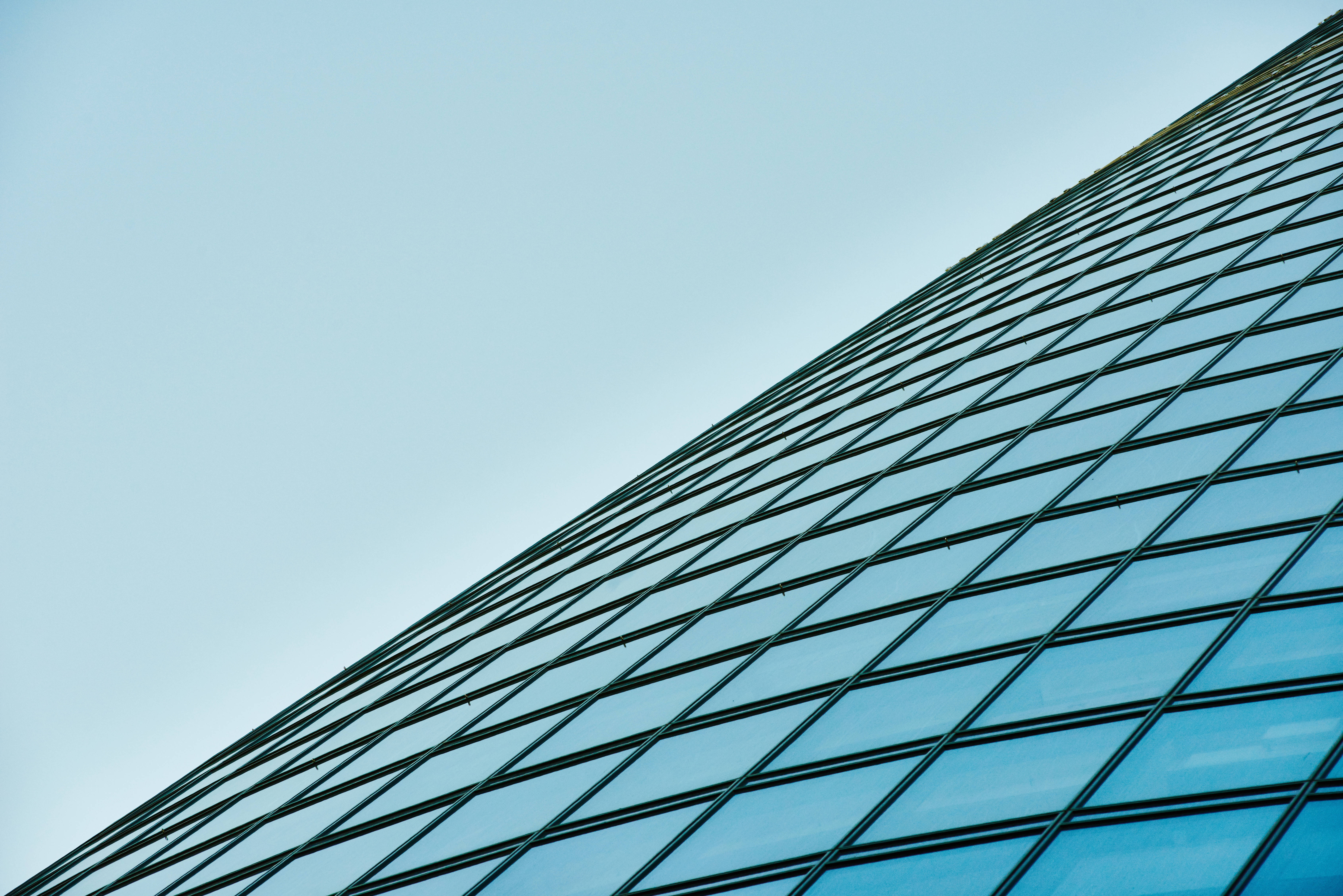 Skyscraper 桌布 壁紙 — 低角度拍攝現代玻璃摩天大樓外牆，背景是清澈的淡藍色天空。