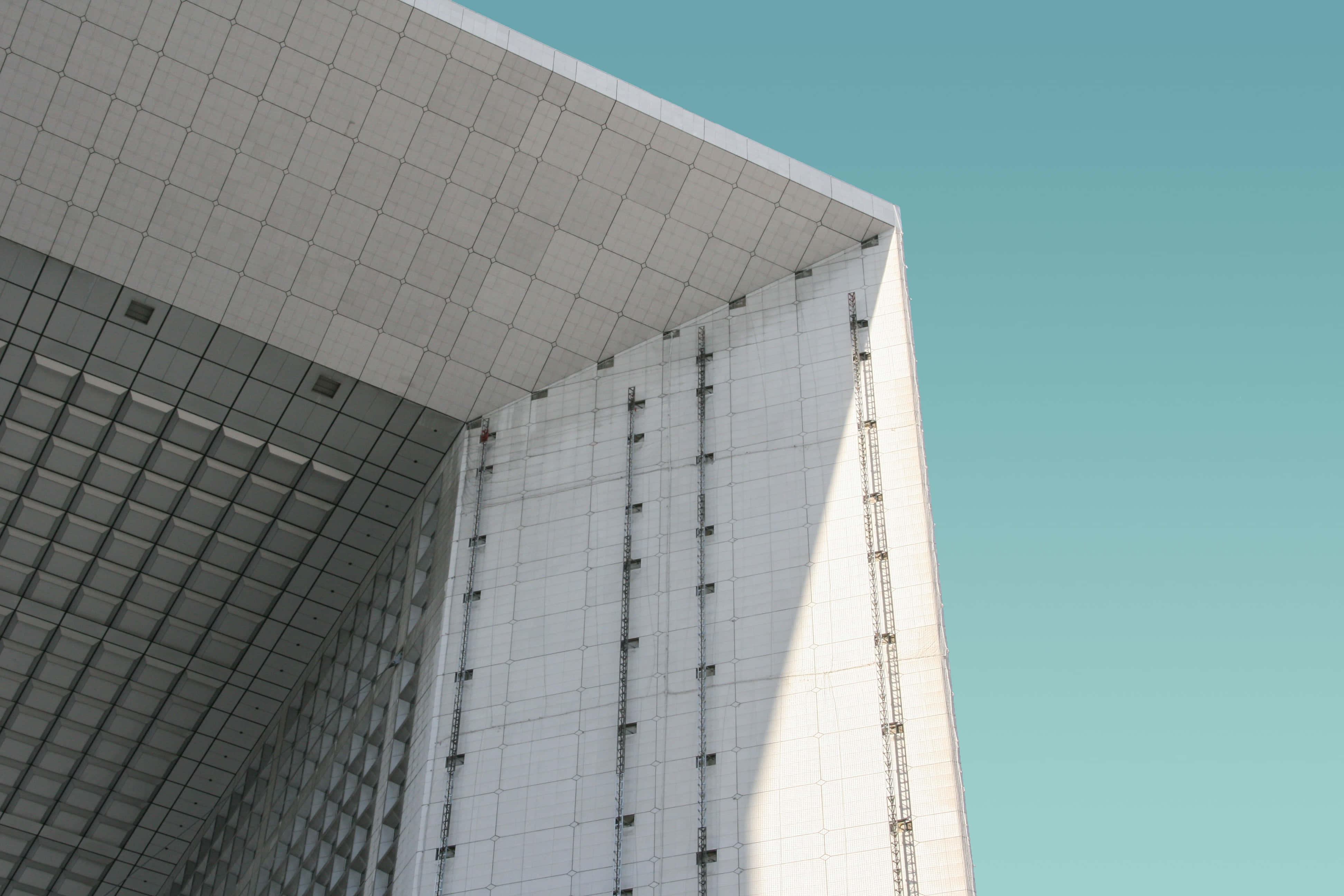 Modernism 桌布 壁紙 — 低角度拍攝現代白色瓷磚建築角落，背景是清澈的青綠色天空，具有銳利的幾何線條和陽光投射的陰影。