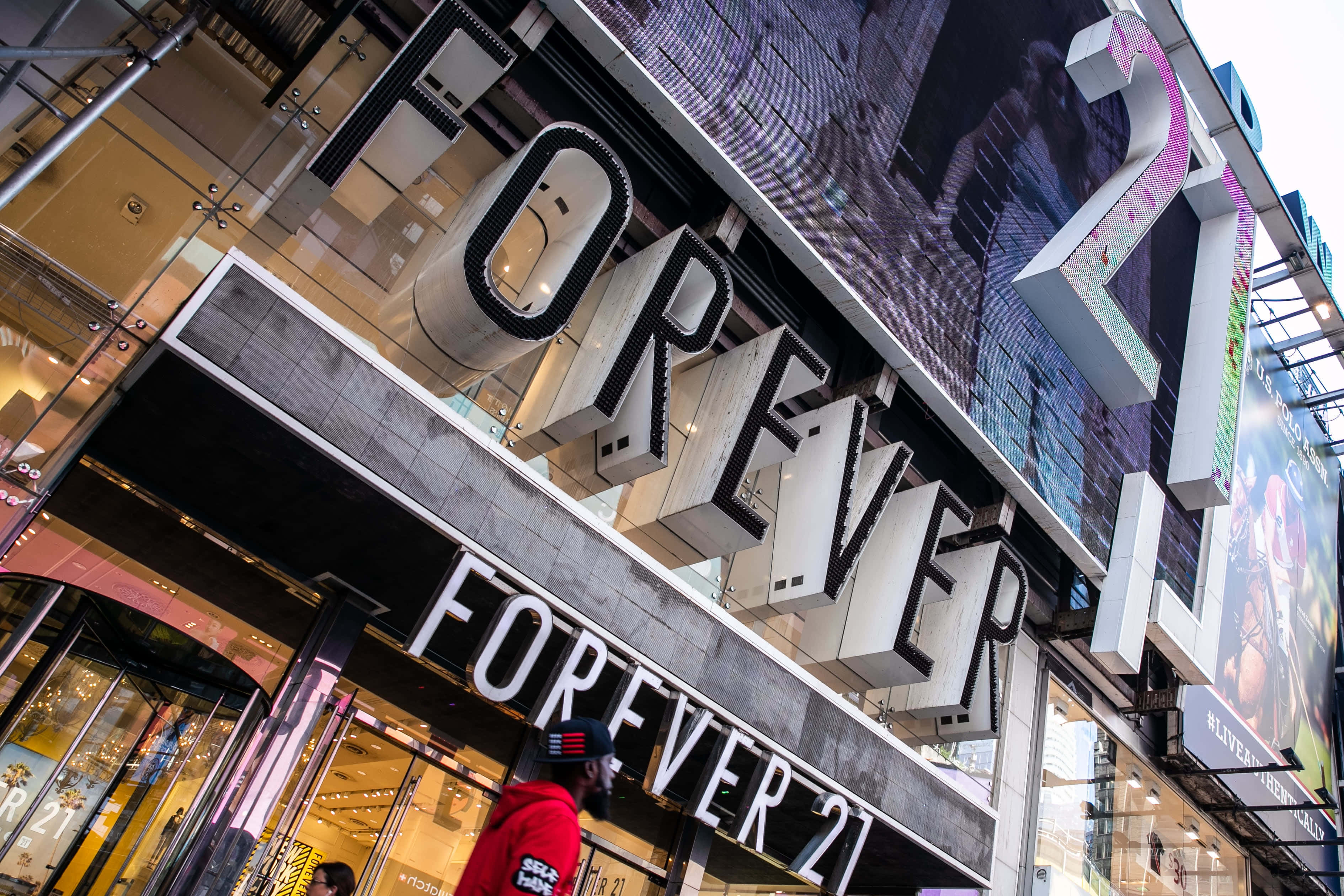 永遠21 桌布 壁紙 — 低角度拍攝的Forever 21店鋪外牆，帶有醒目的白色招牌和玻璃窗，反射城市燈光。