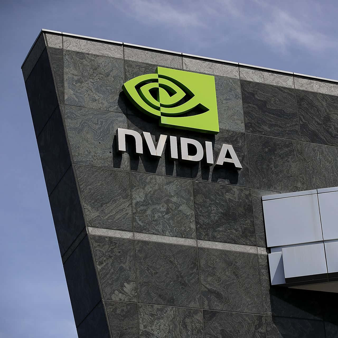nvidia 桌布 壁紙 — 低角度拍攝的NVIDIA標誌，亮綠色和銀色，安裝在深灰色大理石建築外牆上，背景是淡藍色天空。