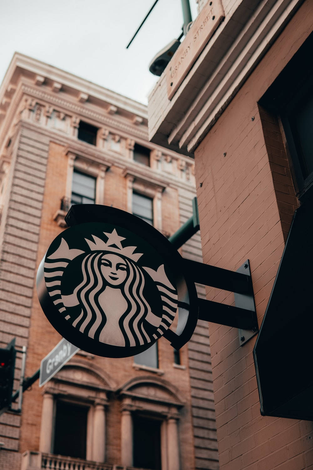 Building 桌布 壁紙 — 低角度拍攝的Starbucks標誌招牌，安裝在磚造建築上，背景為多雲的天空。