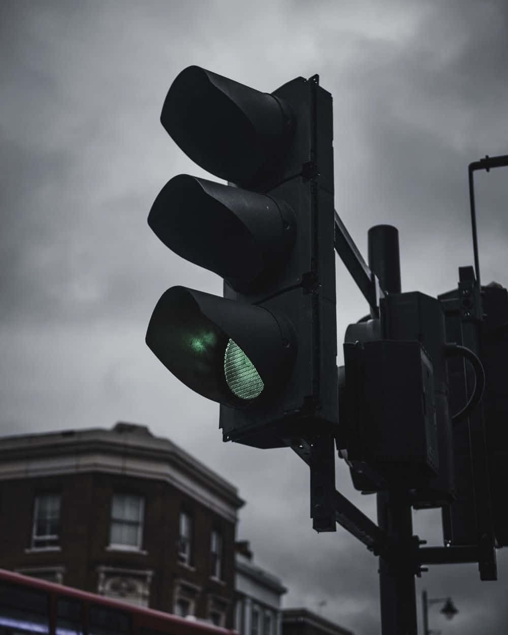 Stop Light 桌布 壁紙 — 低角度拍攝的交通號誌，在陰沉多雲的天空和磚造建築背景下發出綠光。