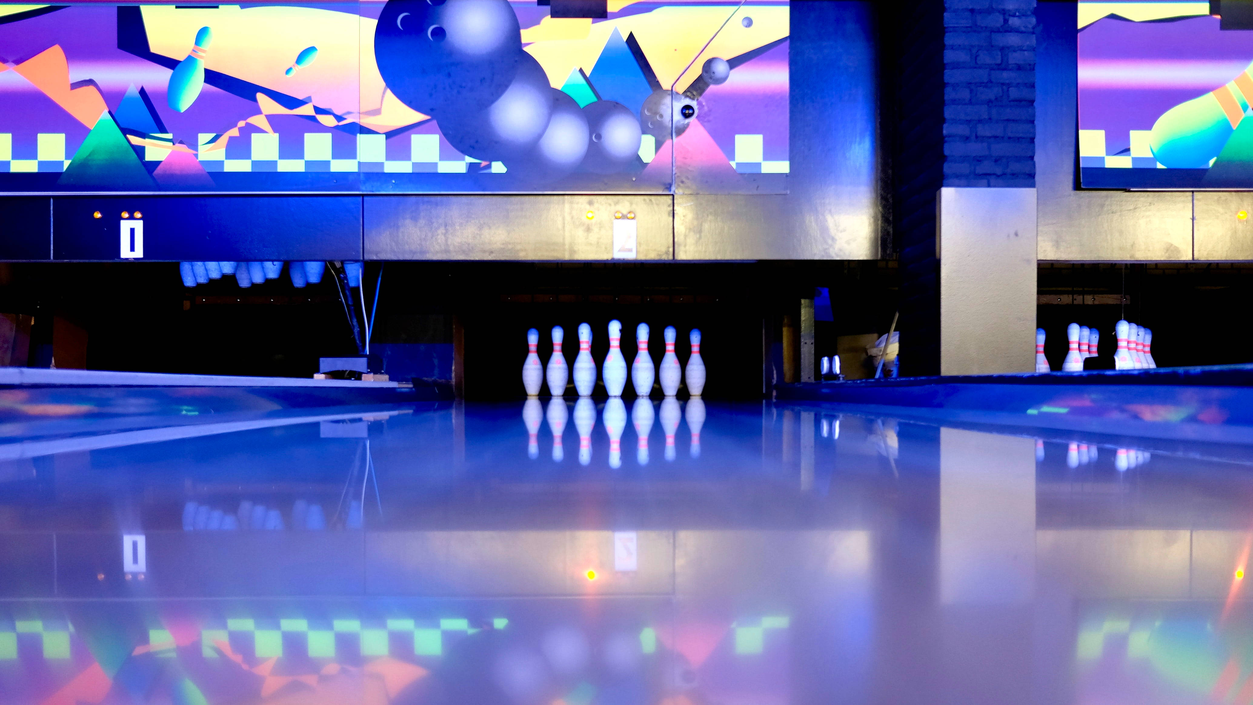 Bowling 桌布 壁紙 — 低角度拍攝的保齡球道，上方有色彩繽紛的數位壁畫，在充滿活力的霓虹燈下。