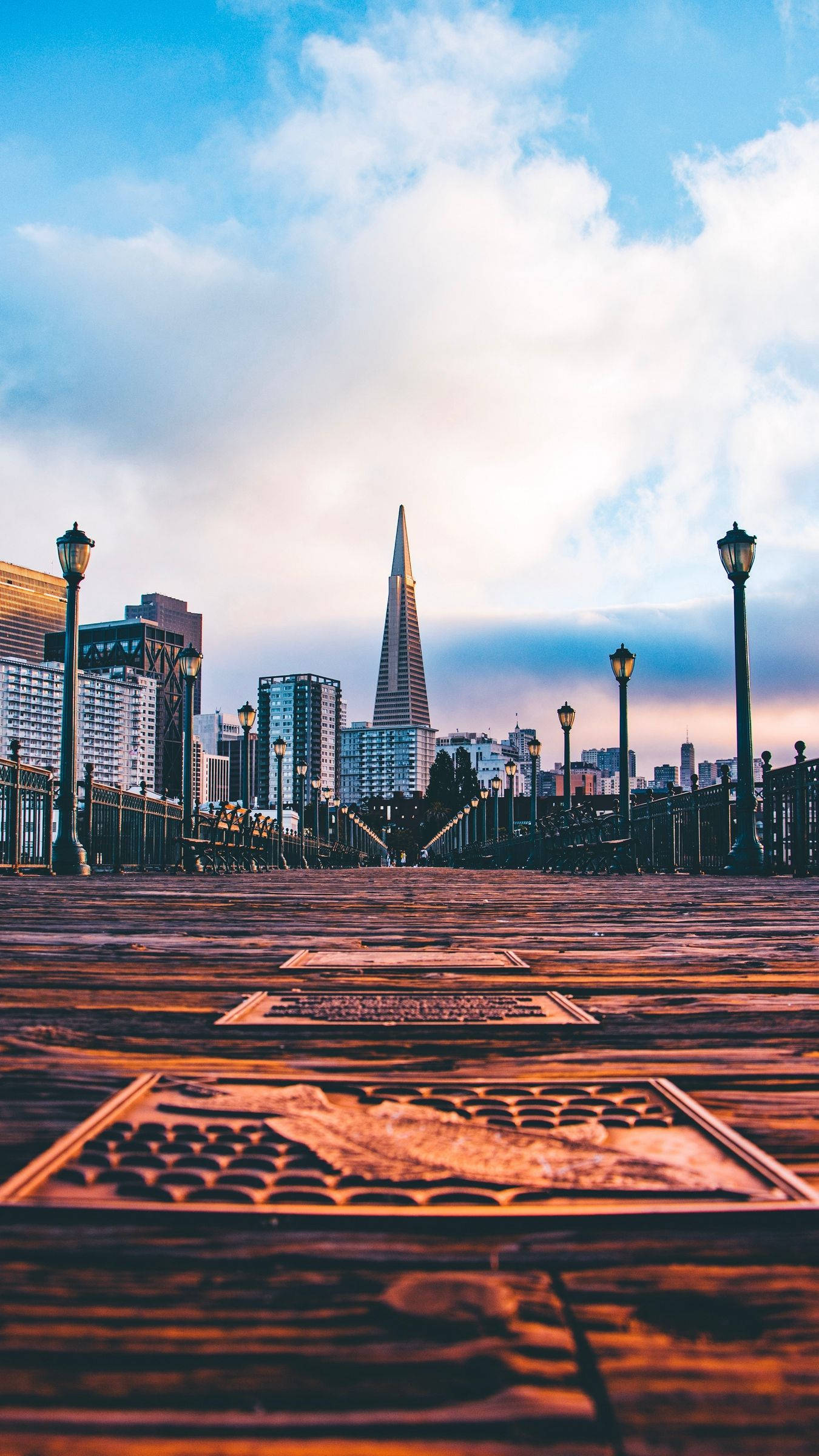 san francisco iPhone 桌布 壁紙 — 低角度拍攝的木製碼頭，通往舊金山日落時分的天際線，泛美金字塔在溫暖的光線中閃耀。