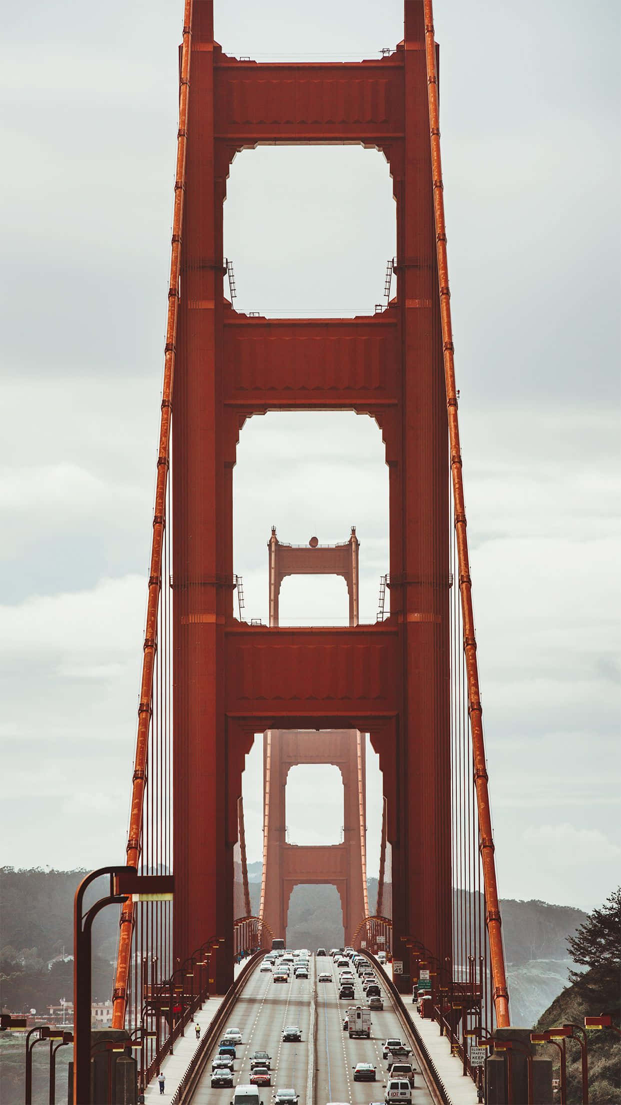 bridge 桌布 壁紙 — 低角度拍攝的標誌性紅色金門大橋，在陰天天空下，其高聳的懸索結構下方有繁忙的車流。
