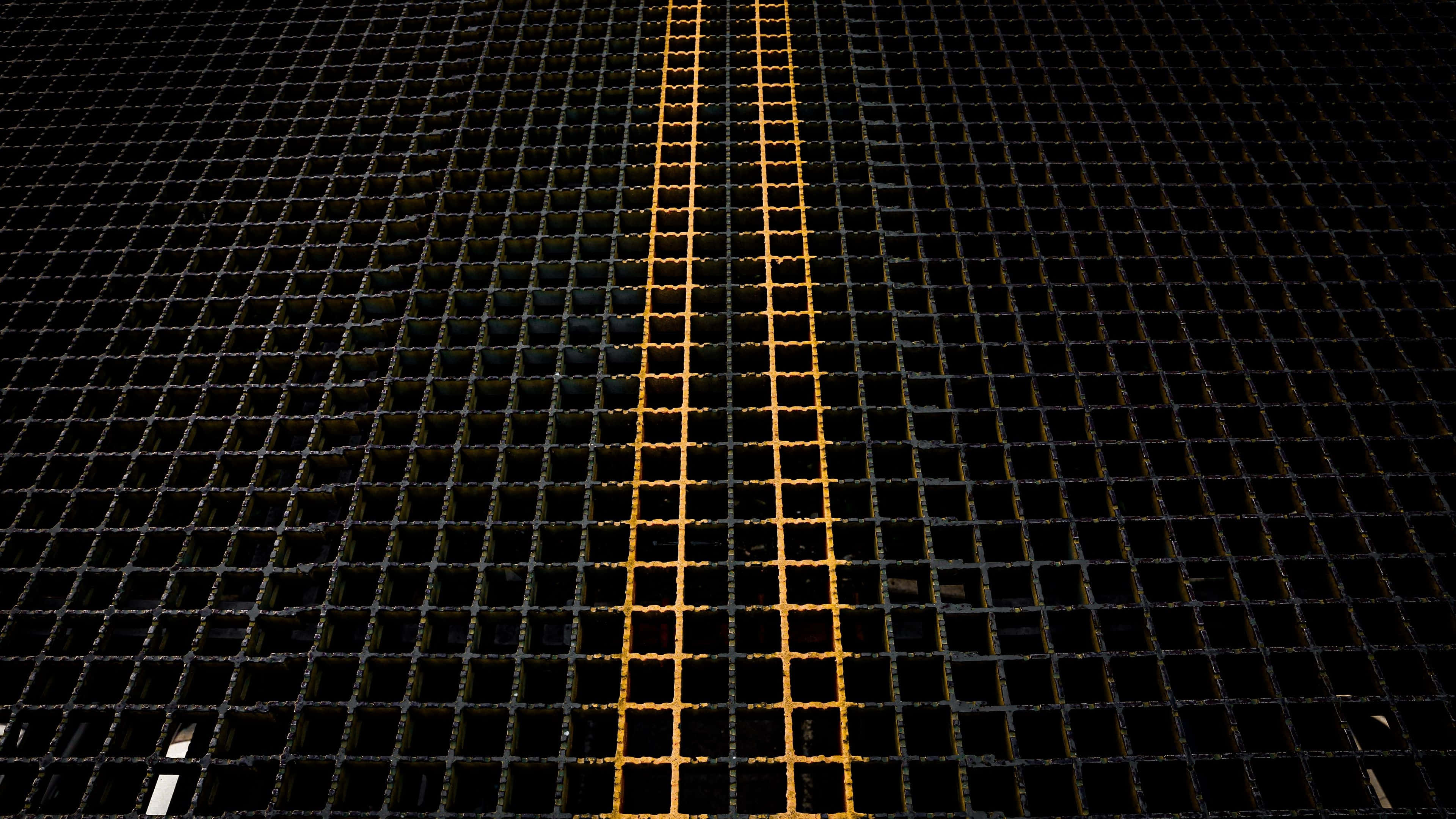 grid 桌布 壁紙 — 低角度拍攝的深色金屬網格地板，中央有一條發光的黃色線條。