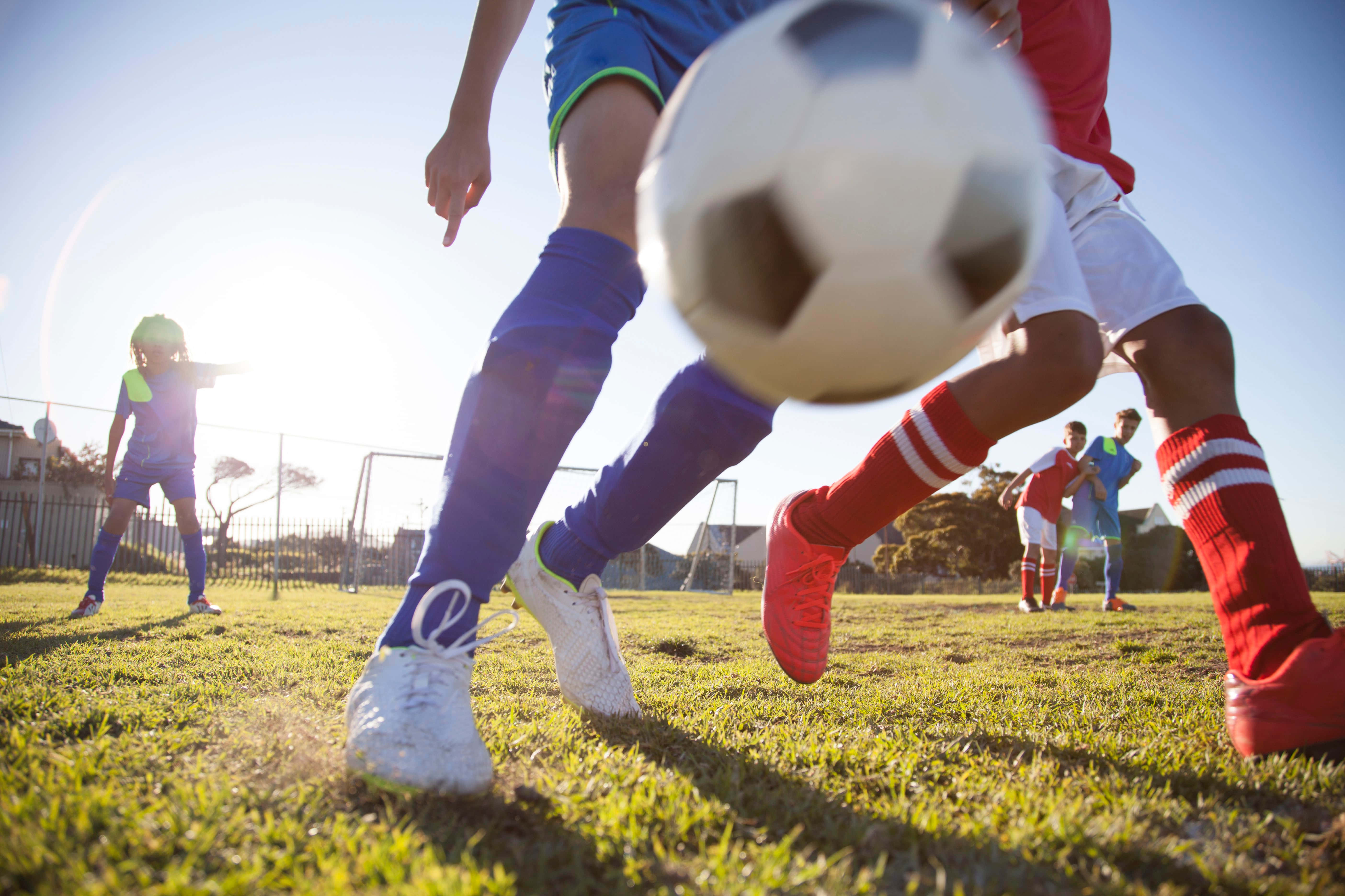Football Profile 桌布 壁紙 — 低角度拍攝足球運動員在草地上行動，帶有太陽耀斑和模糊的球。