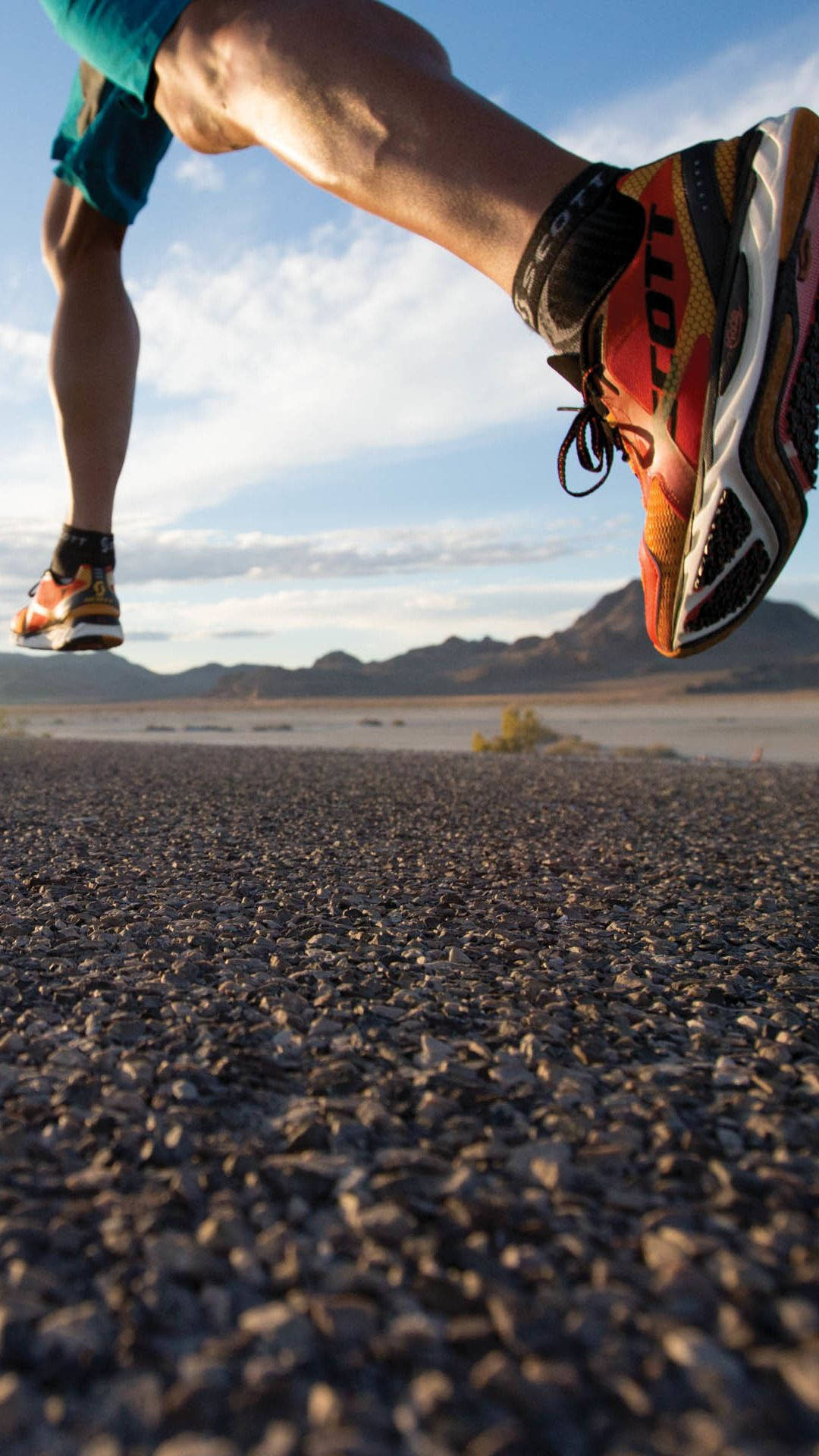 Exercise 桌布 壁紙 — 低角度拍攝跑者在碎石路上跨步中段，背景為沙漠山脈，天空明亮。