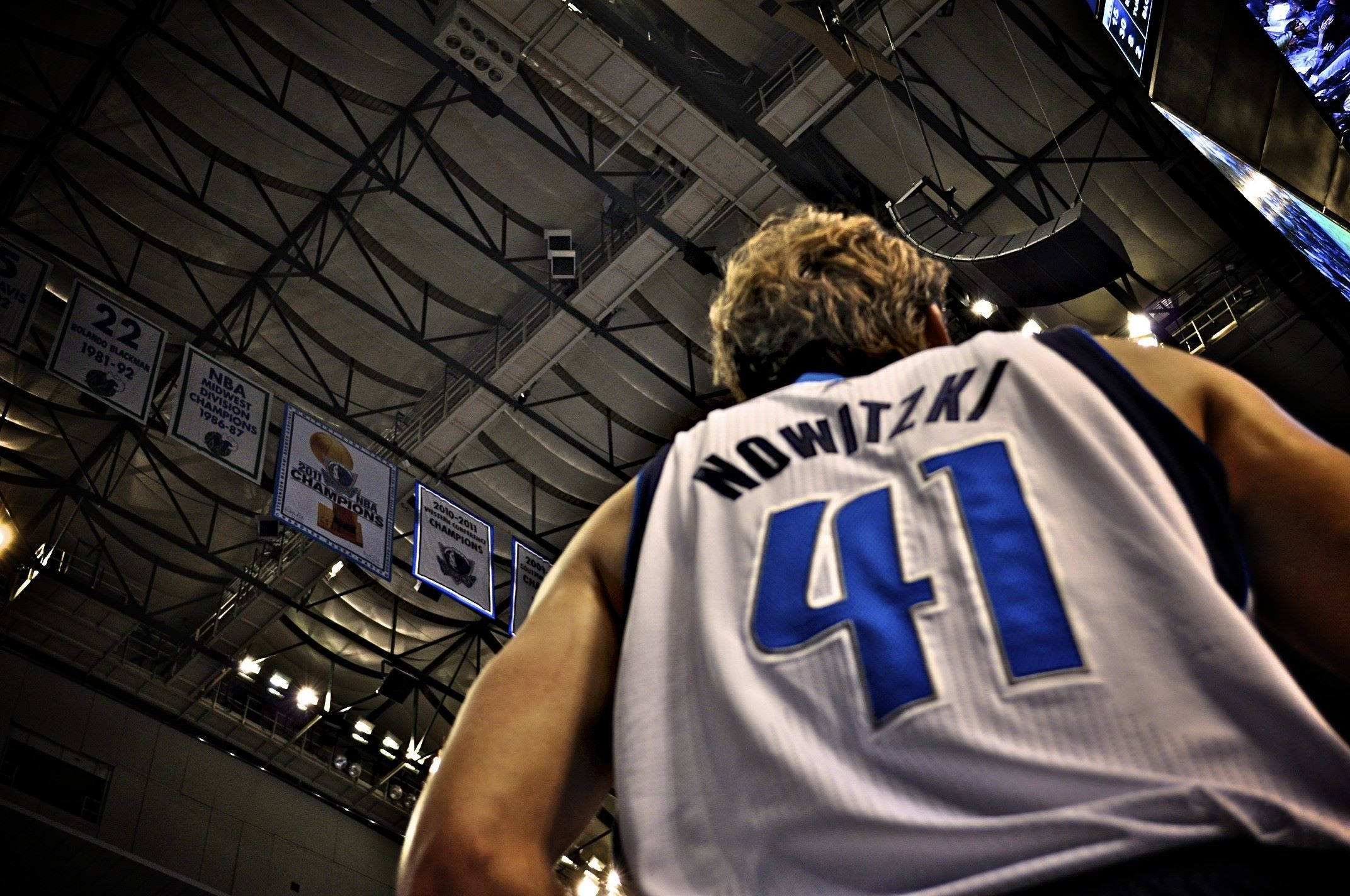 Dirk Nowitzki 桌布 壁紙 — 低角度拍攝身穿達拉斯獨行俠41號球衣的德克·諾維茨基在場館內仰望冠軍旗幟。