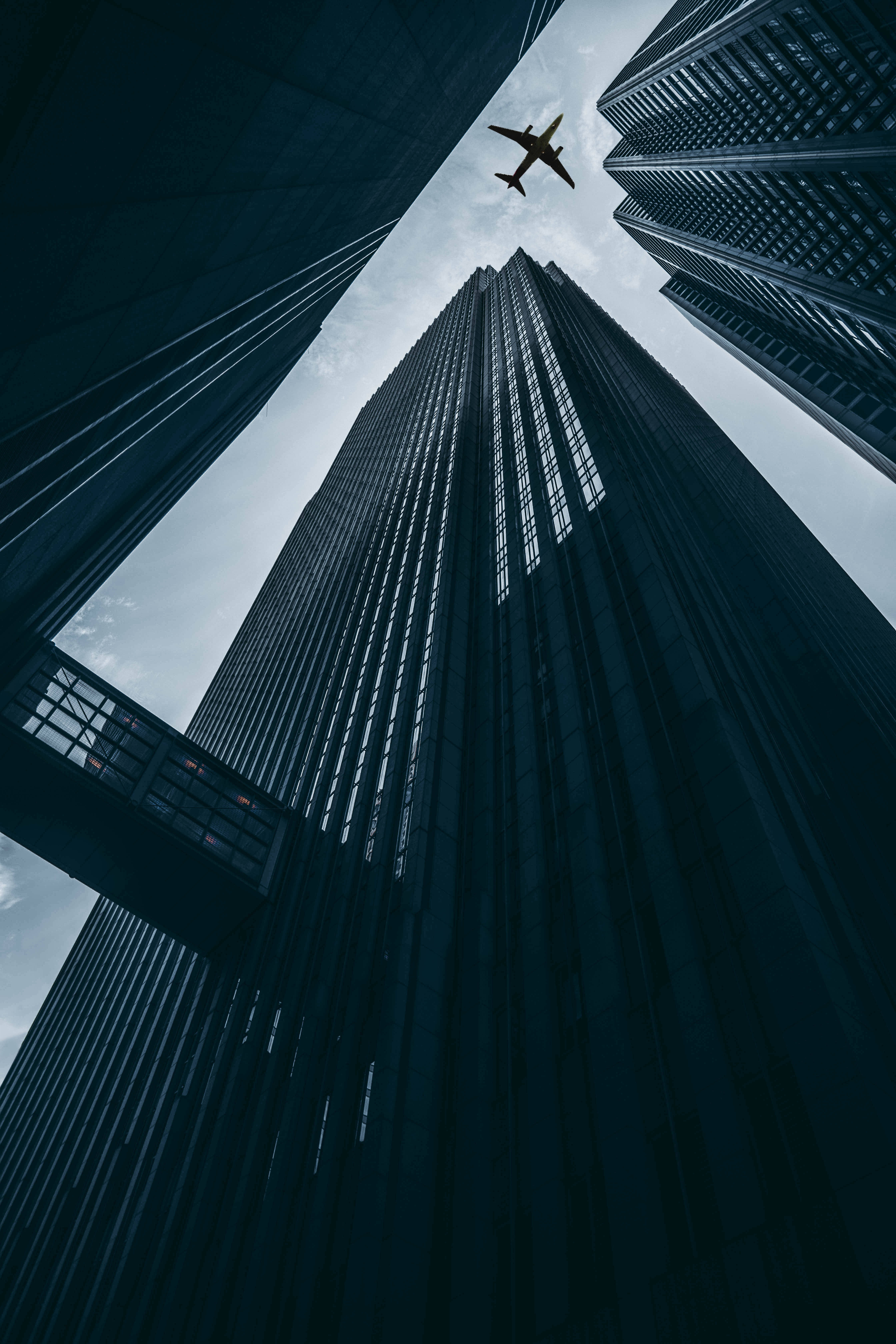 Skyscraper 桌布 壁紙 — 低角度拍攝高聳摩天大樓，框住一架孤獨的飛機飛過多雲的天空。