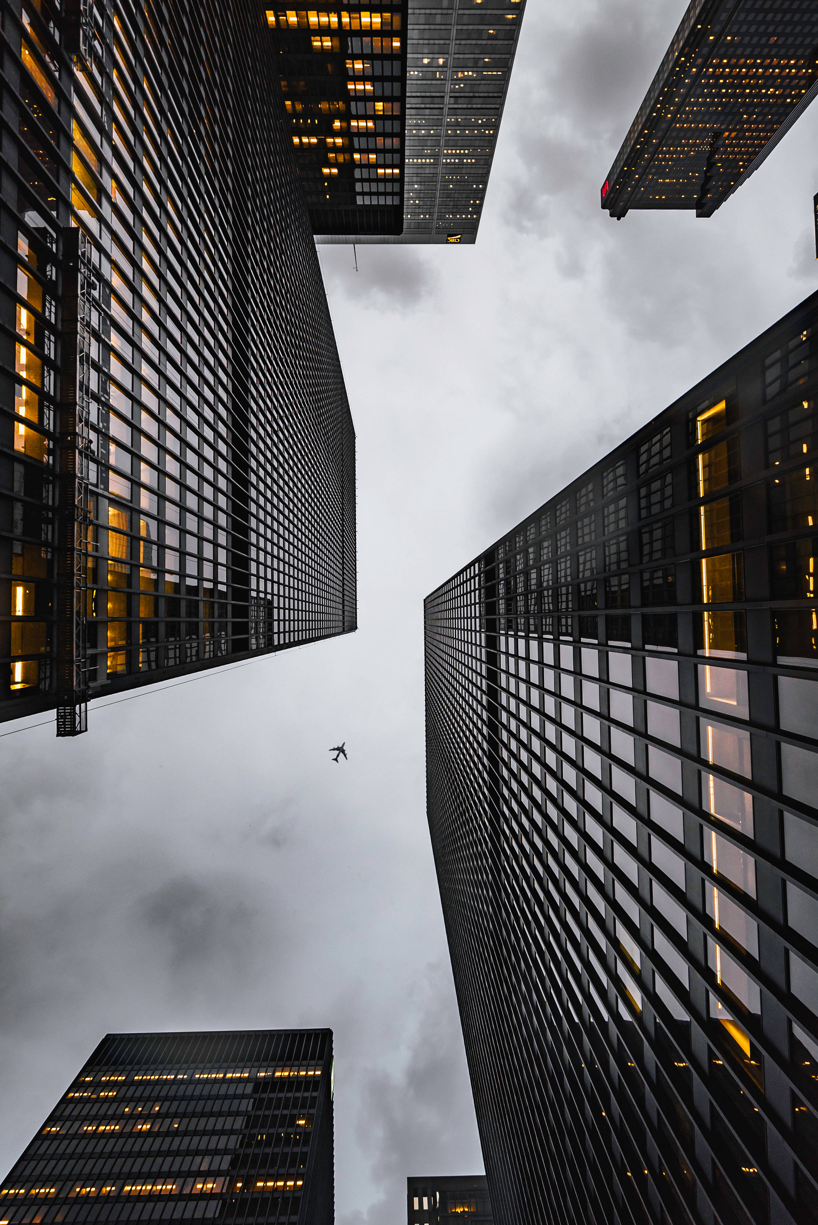 Skyscraper 桌布 壁紙 — 低角度拍攝高聳摩天大樓，窗戶發光，襯托多雲天空，一架小型飛機在它們之間飛過。