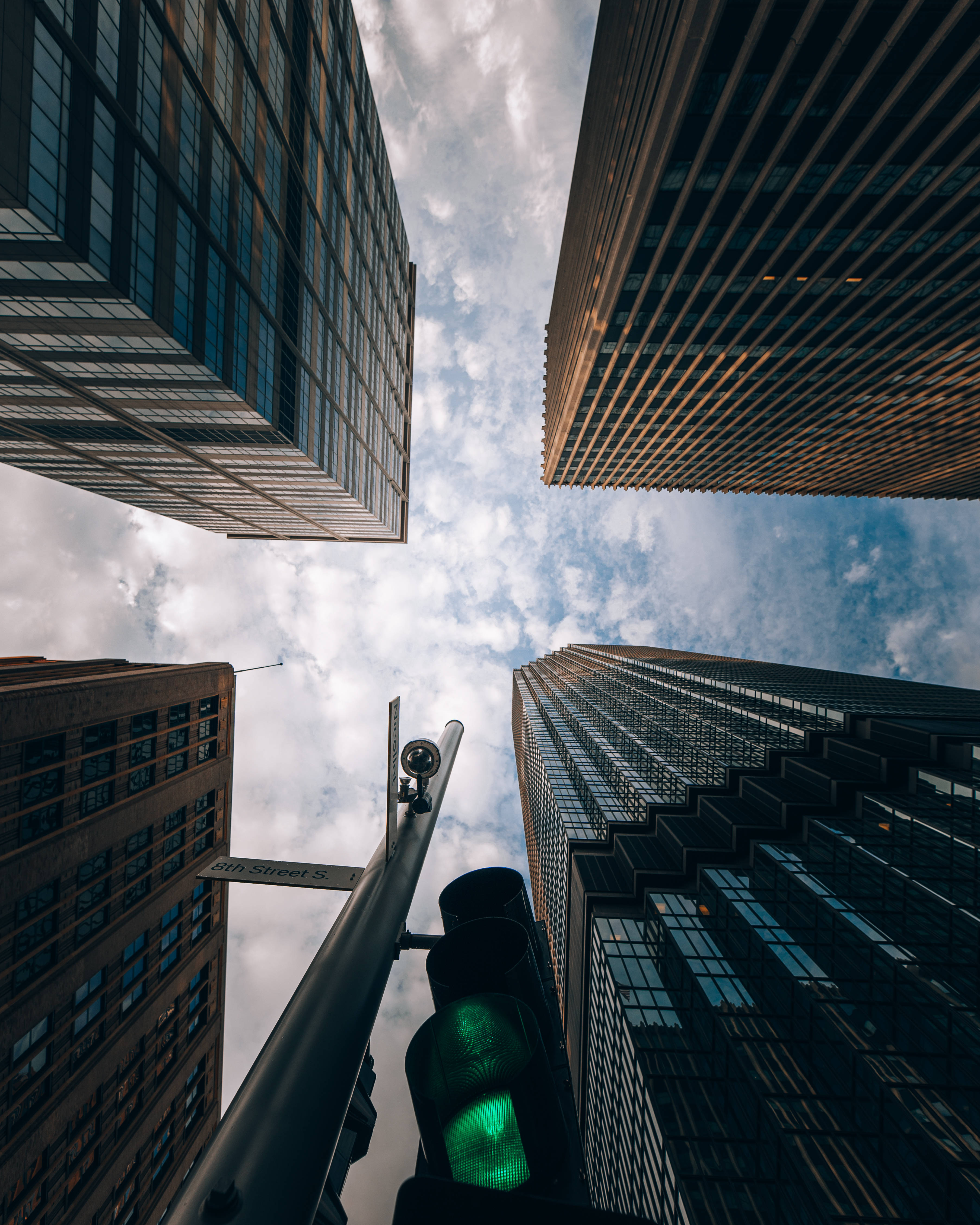 Futuristic City 桌布 壁紙 — 低角度拍攝高聳摩天大樓框住多雲天空，前景有發光綠色交通燈。