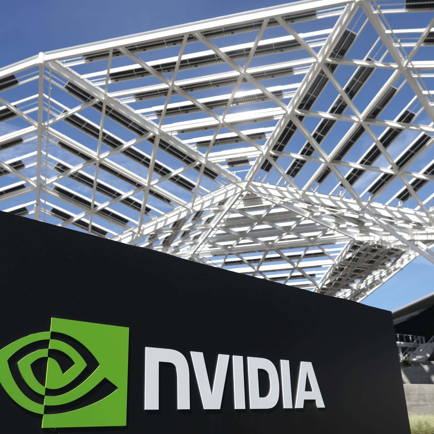 nvidia 桌布 壁紙 — 低角度拍攝黑色NVIDIA標誌，帶有綠色標誌，位於白色幾何屋頂下，背景是晴朗的藍天。