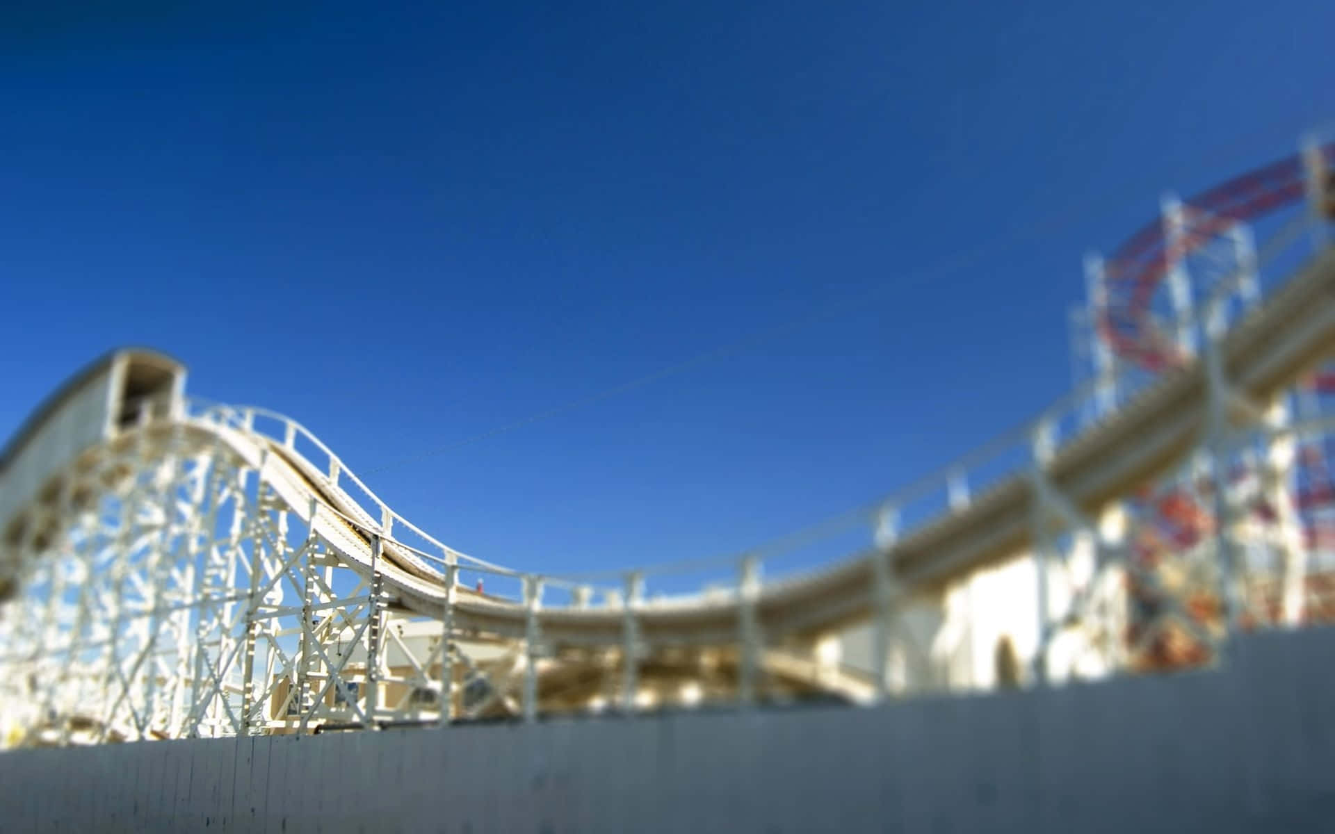 Roller Coaster 桌布 壁紙 — 低角度移軸鏡頭視角，白色木製雲霄飛車軌道在清澈藍天下彎曲。