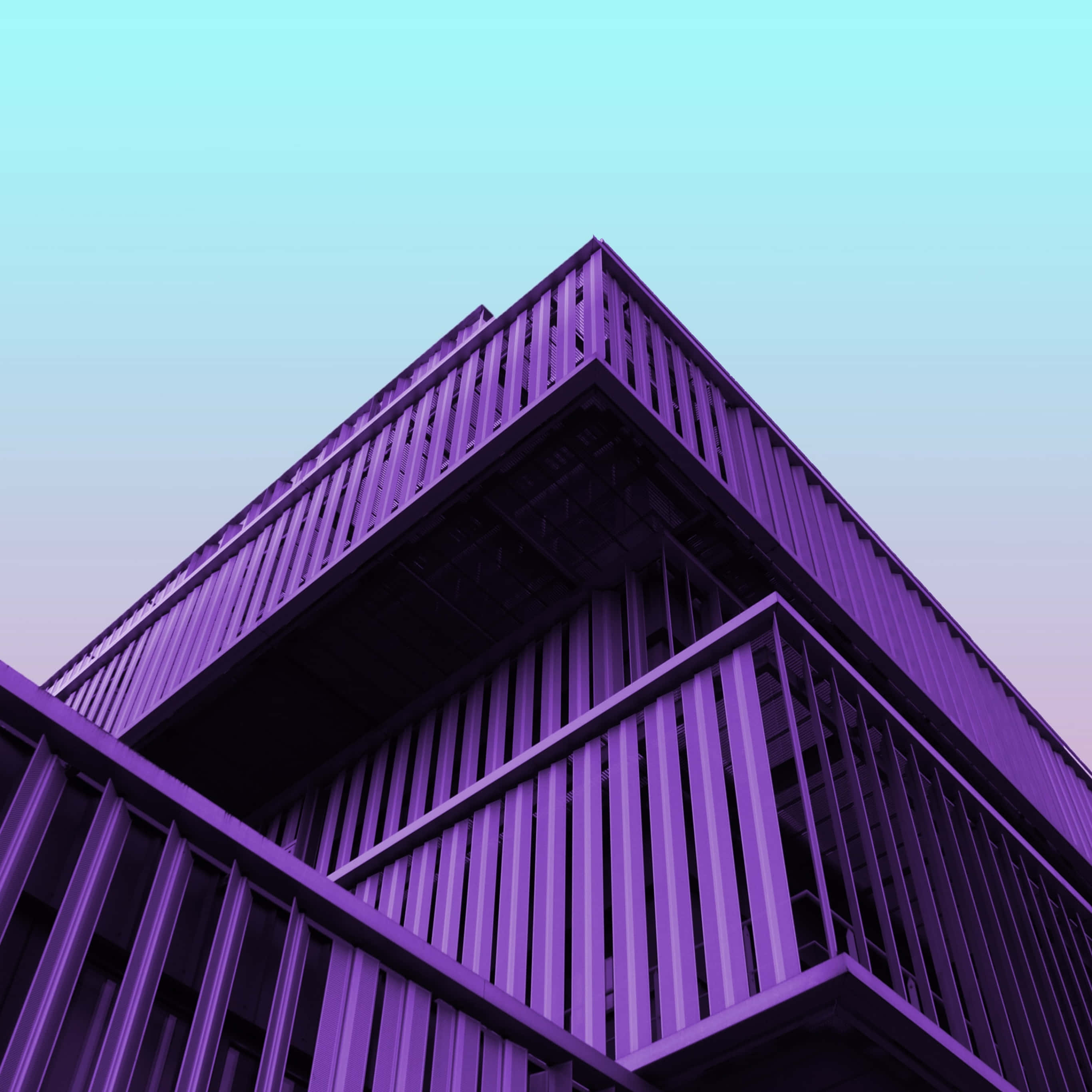 建築 桌布 壁紙 — 低角度觀看一座現代幾何建築，沐浴在充滿活力的紫色光線中，背景是漸變色的天空。