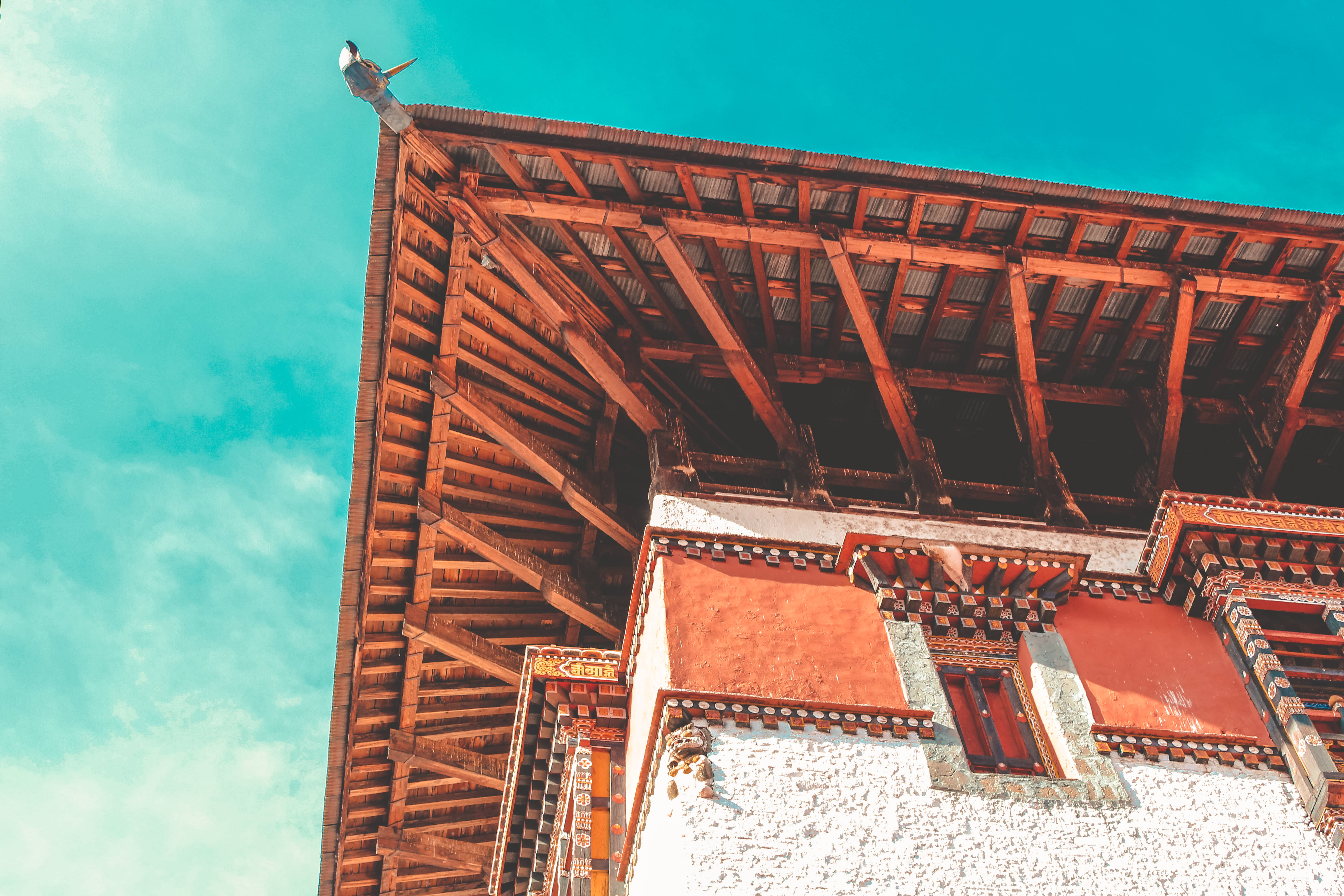 Bhutan 桌布 壁紙 — 低角度觀看傳統不丹建築，外露木樑和白色石牆，襯托著充滿活力的綠松色天空。