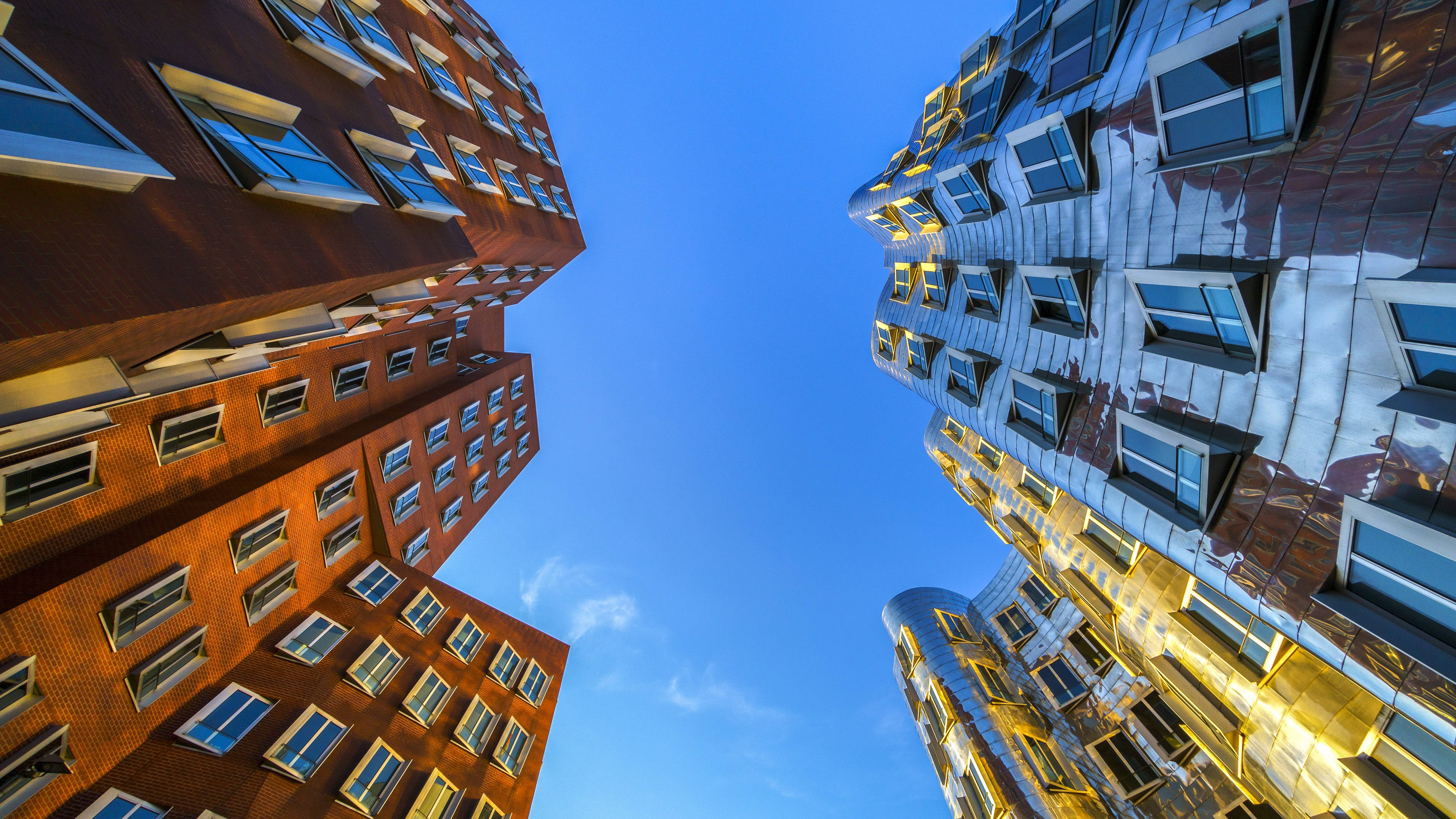 Modern 桌布 壁紙 — 低角度觀看兩座對比鮮明的現代建築，一座磚造，一座鏡面，在清澈的藍天下向上彎曲。