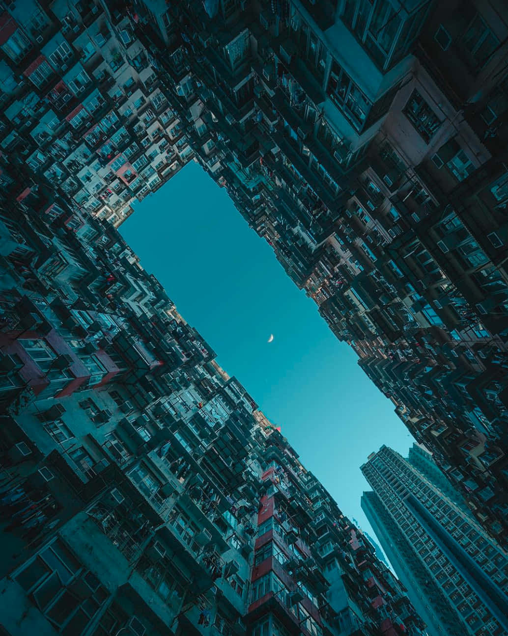 城市 桌布 壁紙 — 低角度觀看密集的城市建築物，框住一片清澈的藍綠色天空，伴隨著一彎新月。