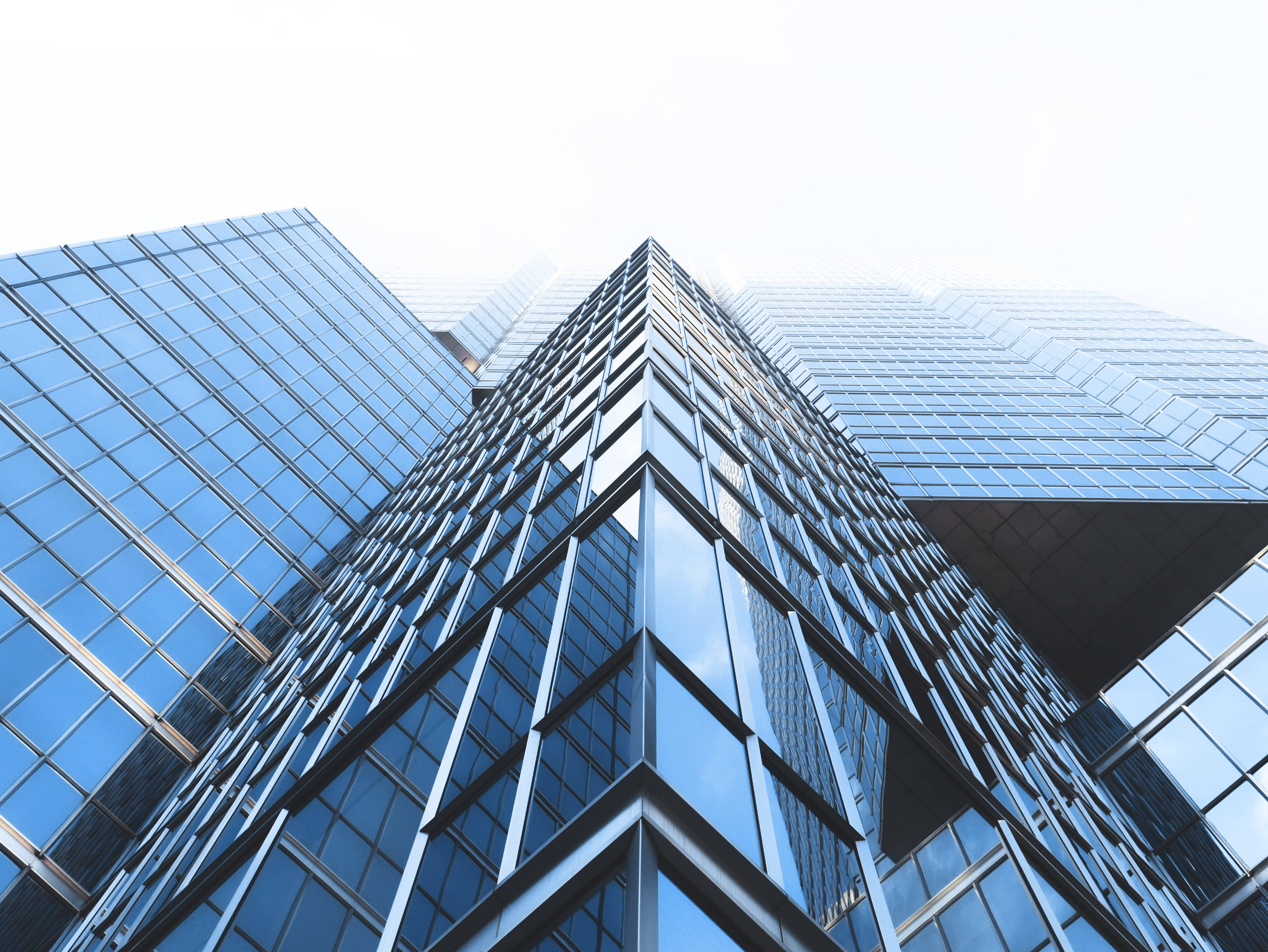 Skyscraper 桌布 壁紙 — 低角度觀看現代玻璃摩天大樓，在明亮的白色天空下反射藍天和白雲。