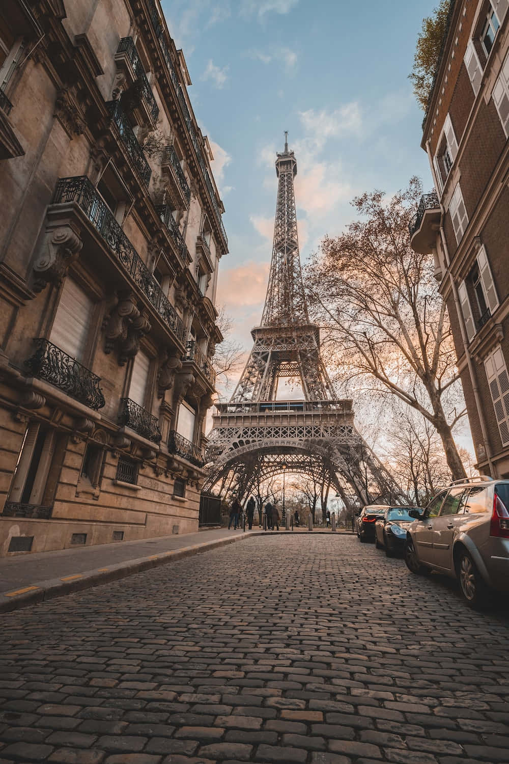 France 桌布 壁紙 — 低角度觀看艾菲爾鐵塔在歷史悠久的巴黎建築之間升起，背景是柔和的金色日落天空。