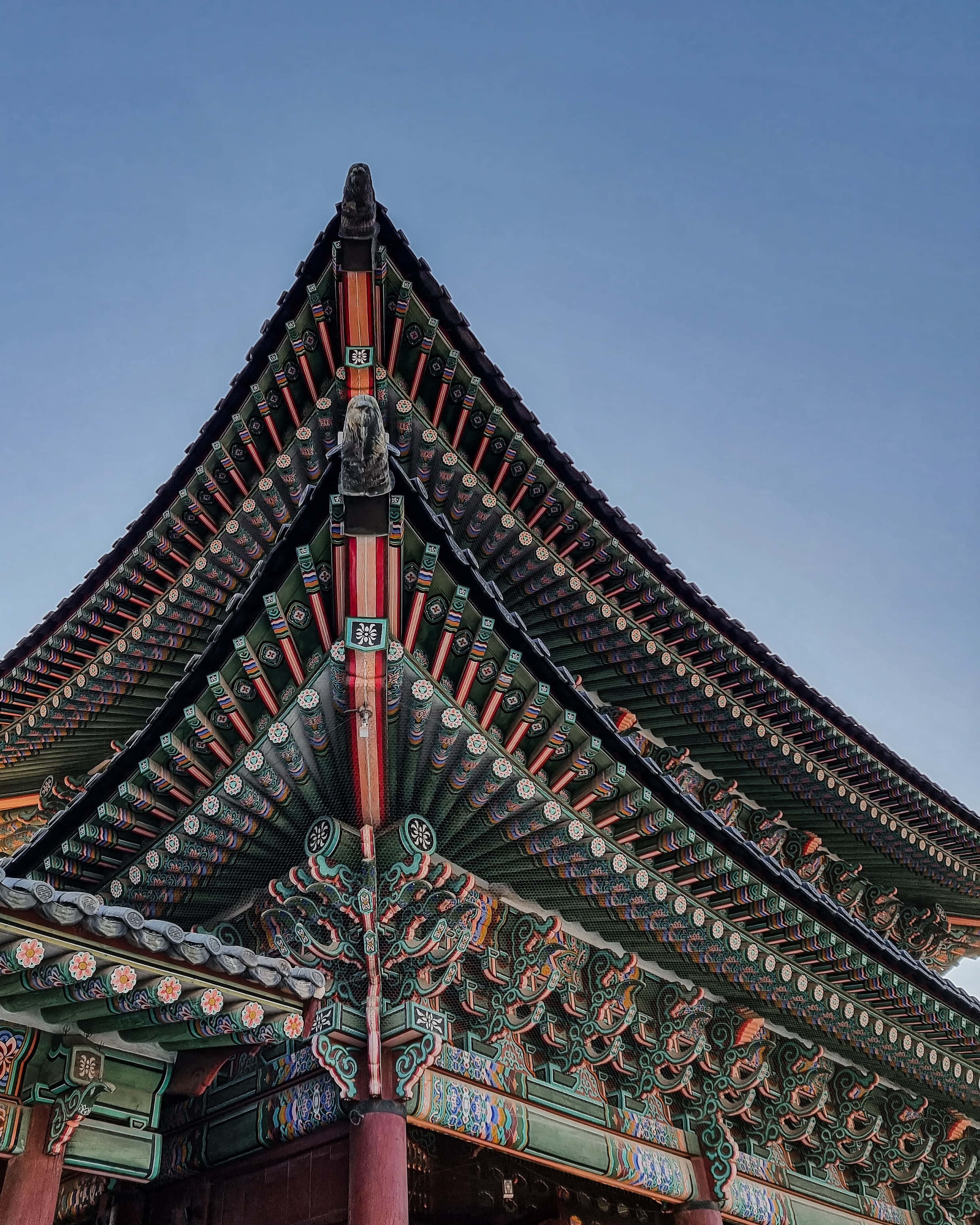 建築 桌布 壁紙 — 低角度觀看裝飾華麗的傳統韓國寺廟屋頂，在清澈的藍天下呈現複雜的綠色、紅色和金色細節。