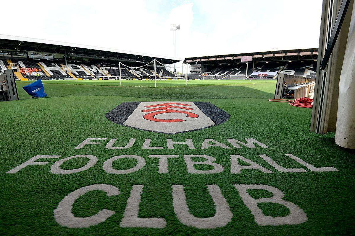Football Field 桌布 壁紙 — 低角度觀看足球場，翠綠草地上繪有「FULHAM FOOTBALL CLUB」及會徽，周圍是空無一人的球場看台，陽光普照。