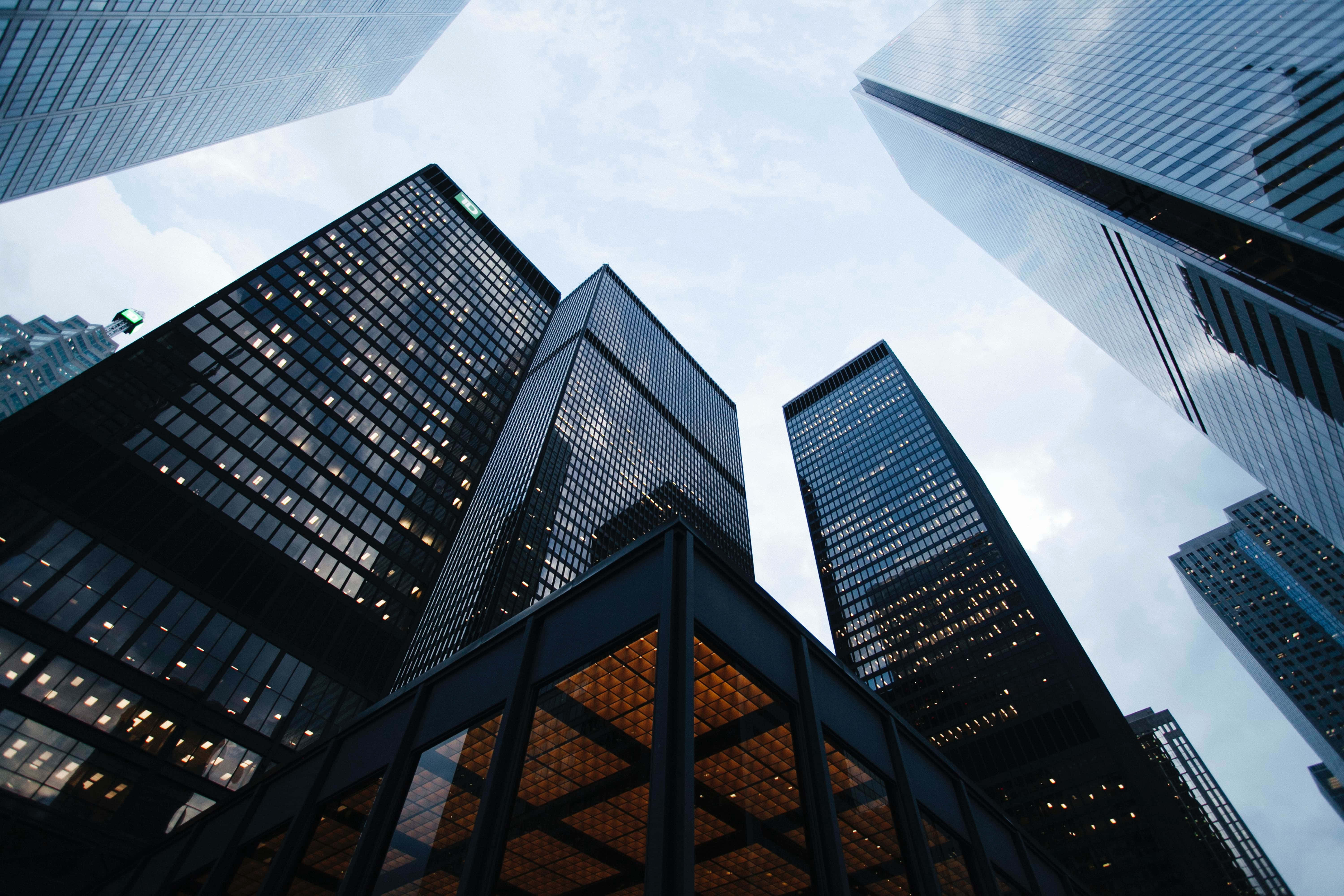 Buildings 桌布 壁紙 — 低角度觀看高聳的玻璃摩天大樓刺穿多雲的天空，溫暖的室內燈光在冷藍色調中閃耀。