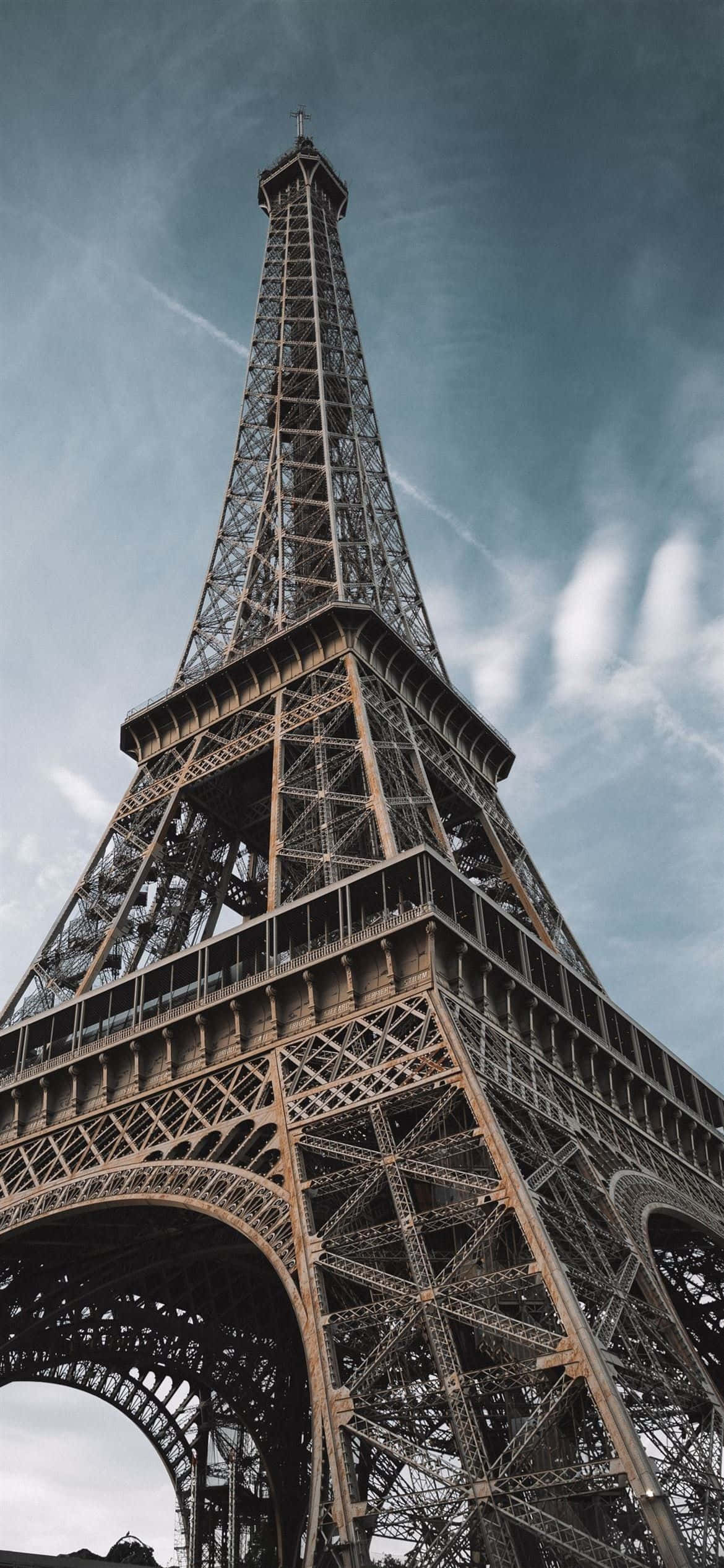 Eiffel Tower 桌布 壁紙 — 低角度觀賞艾菲爾鐵塔複雜的鐵格結構，背景是帶有縷縷白雲的憂鬱藍天。
