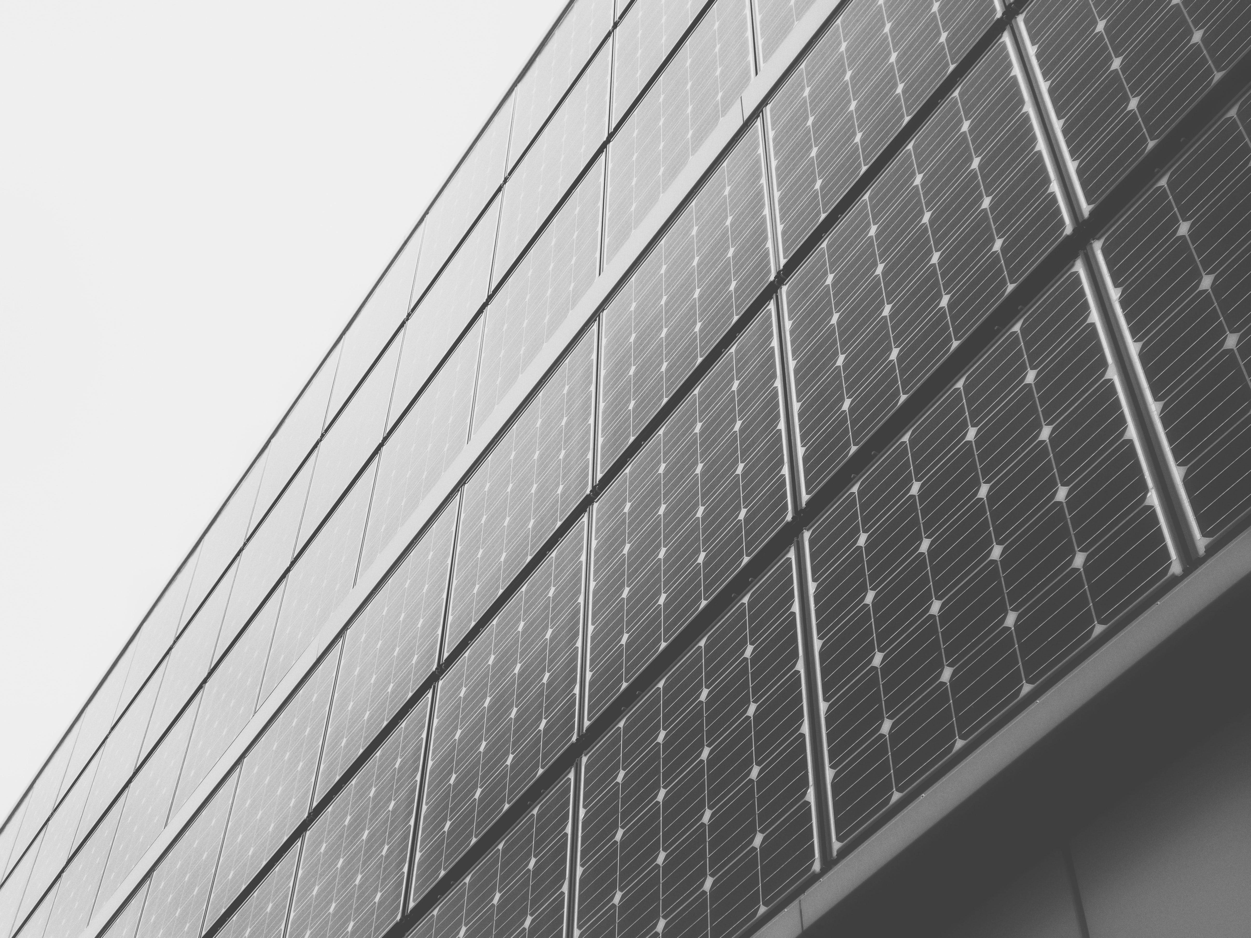 黑白 桌布 壁紙 — 低角度黑白拍攝，太陽能板覆蓋建築物外牆，天空多雲。