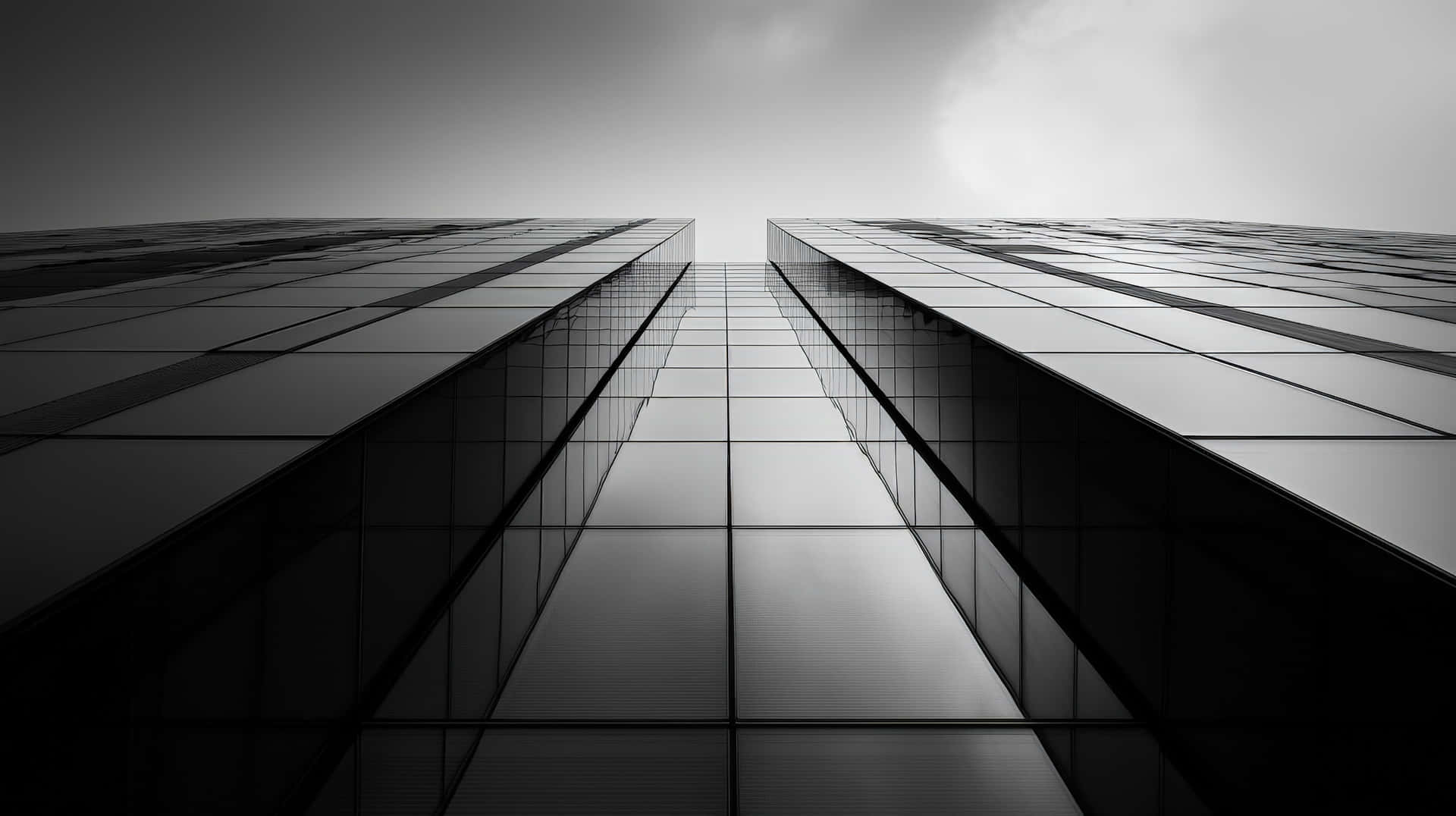 Black and White Skyscraper with Reflective Glass Panels Showing Dramatic Perspective 壁紙 — 低角度黑白照片，兩座玻璃摩天大樓向明亮的天空匯聚。