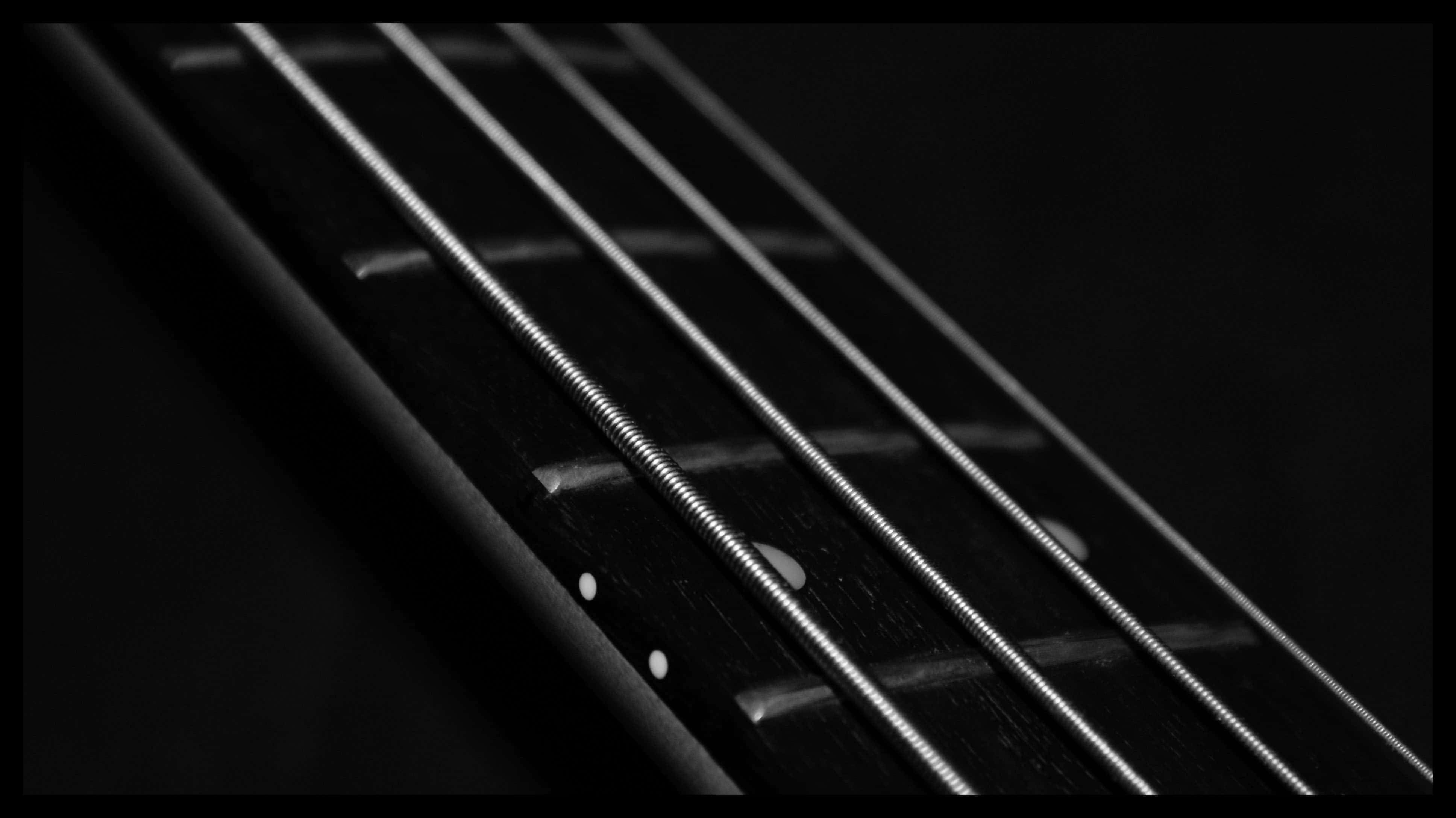 Bass Guitar 桌布 壁紙 — 低音吉他指板特寫，帶有金屬弦線和嵌入式圓點標記，背景為純黑色。