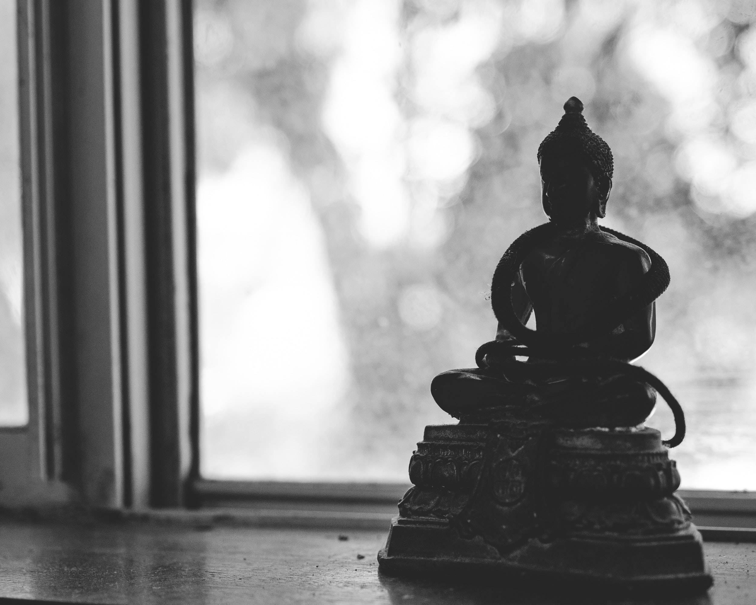 black buddha 桌布 壁紙 — 佛像剪影靜靜地坐在窗台上，背景是柔和模糊的日光。