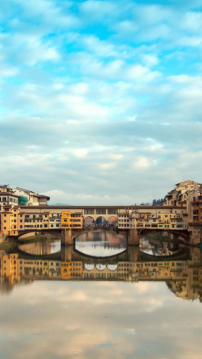 Blue Sky 桌布 壁紙 — 佛羅倫斯歷史悠久的舊橋（Ponte Vecchio）在平靜的阿諾河上美麗地倒映，柔和的藍天中散佈著雲朵。