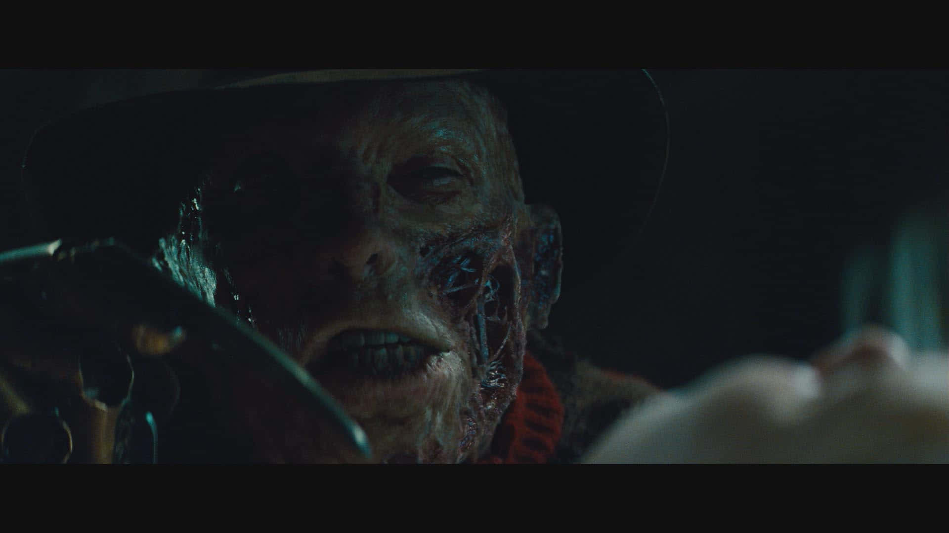 Freddy Krueger 桌布 壁紙 — 佛萊迪·克魯格特寫，臉上帶有疤痕，戴著利刃手套，處於昏暗場景中。