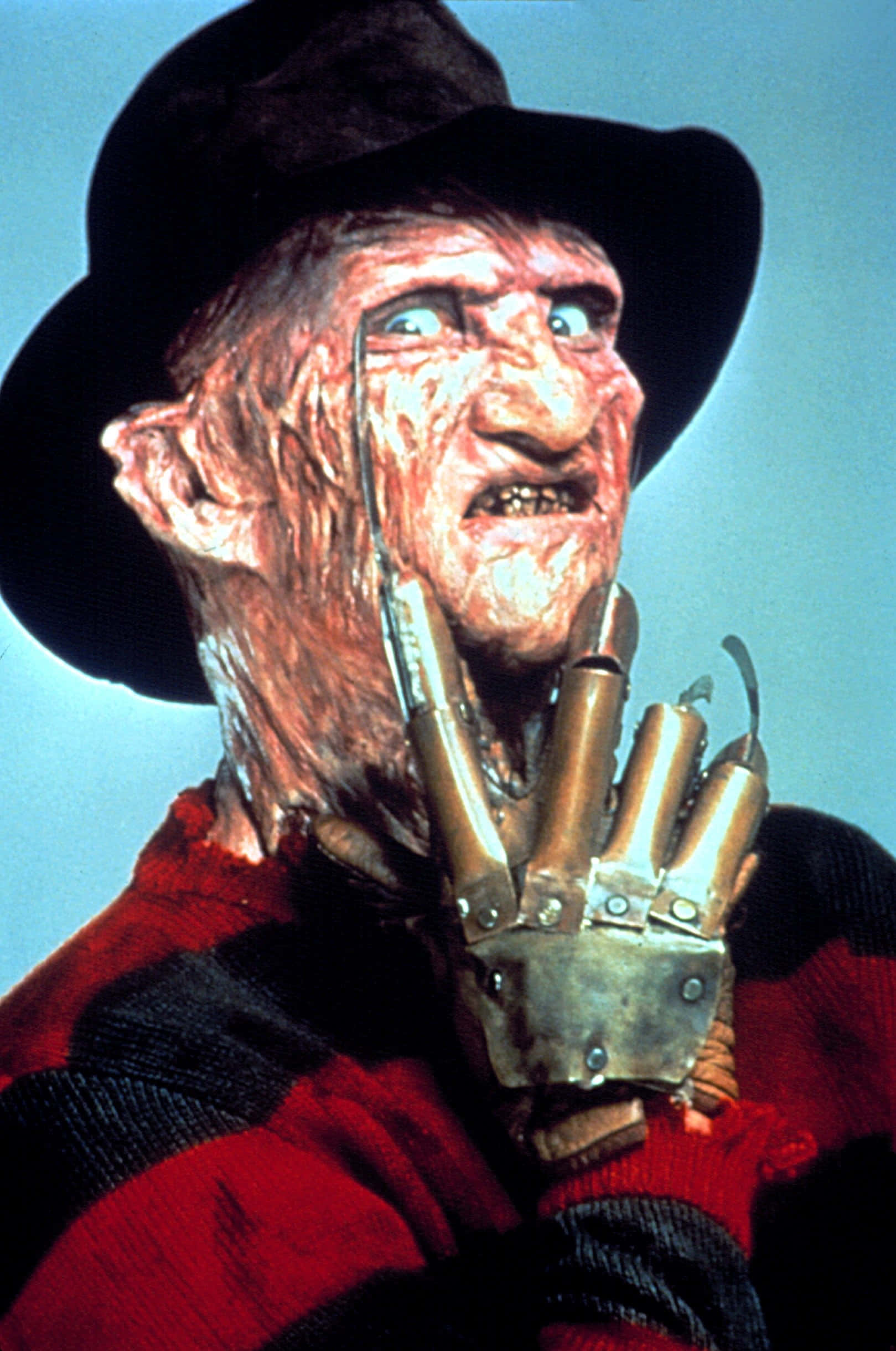 Freddy Krueger 桌布 壁紙 — 佛萊迪·克魯格的特寫，露出兇惡的笑容，戴著佈滿刀片的手套，背景是淡藍色。