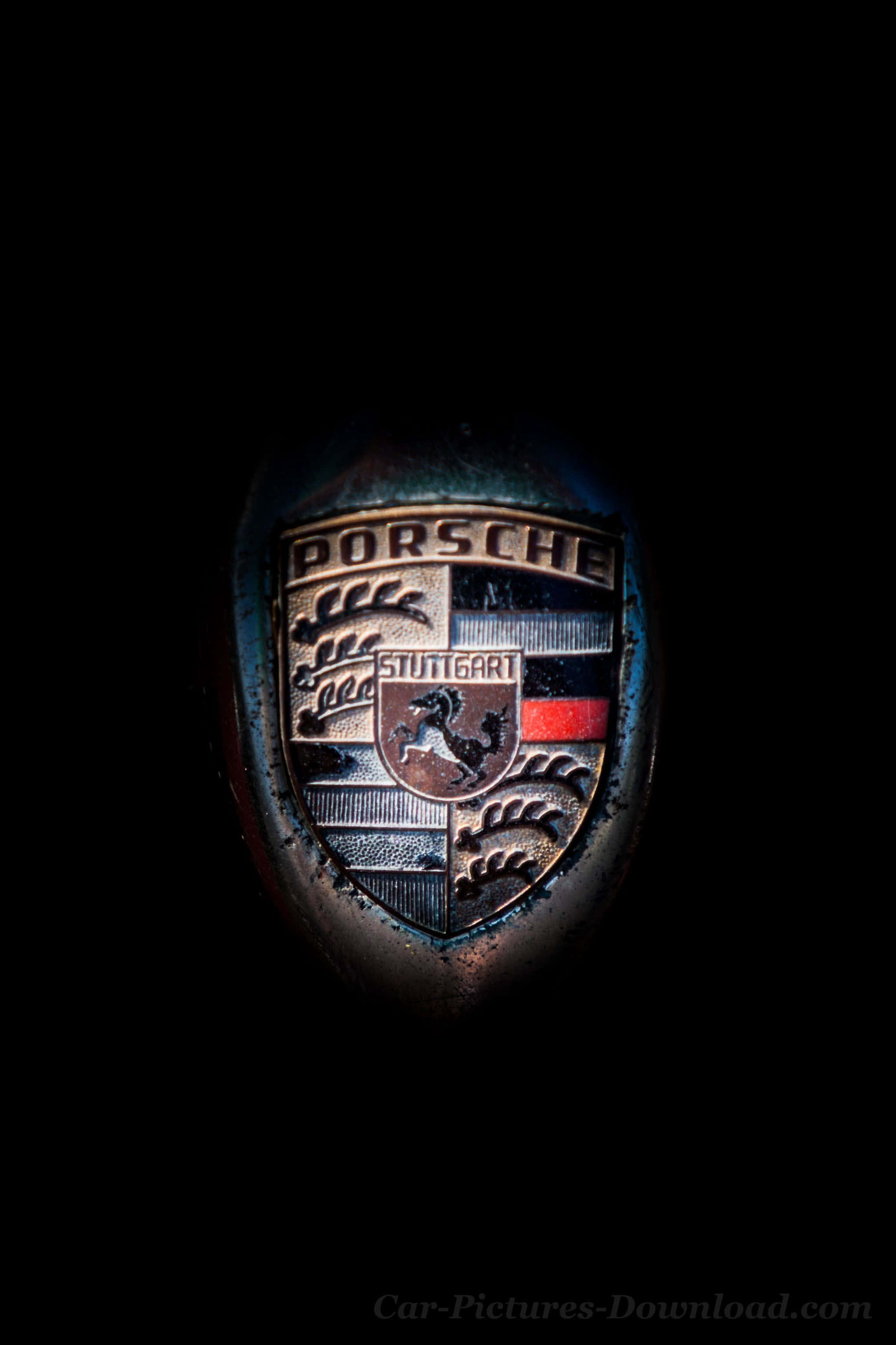 Porsche iPhone 桌布 壁紙 — 保時捷標誌在漆黑背景下，於戲劇性聚光燈下閃耀的特寫。