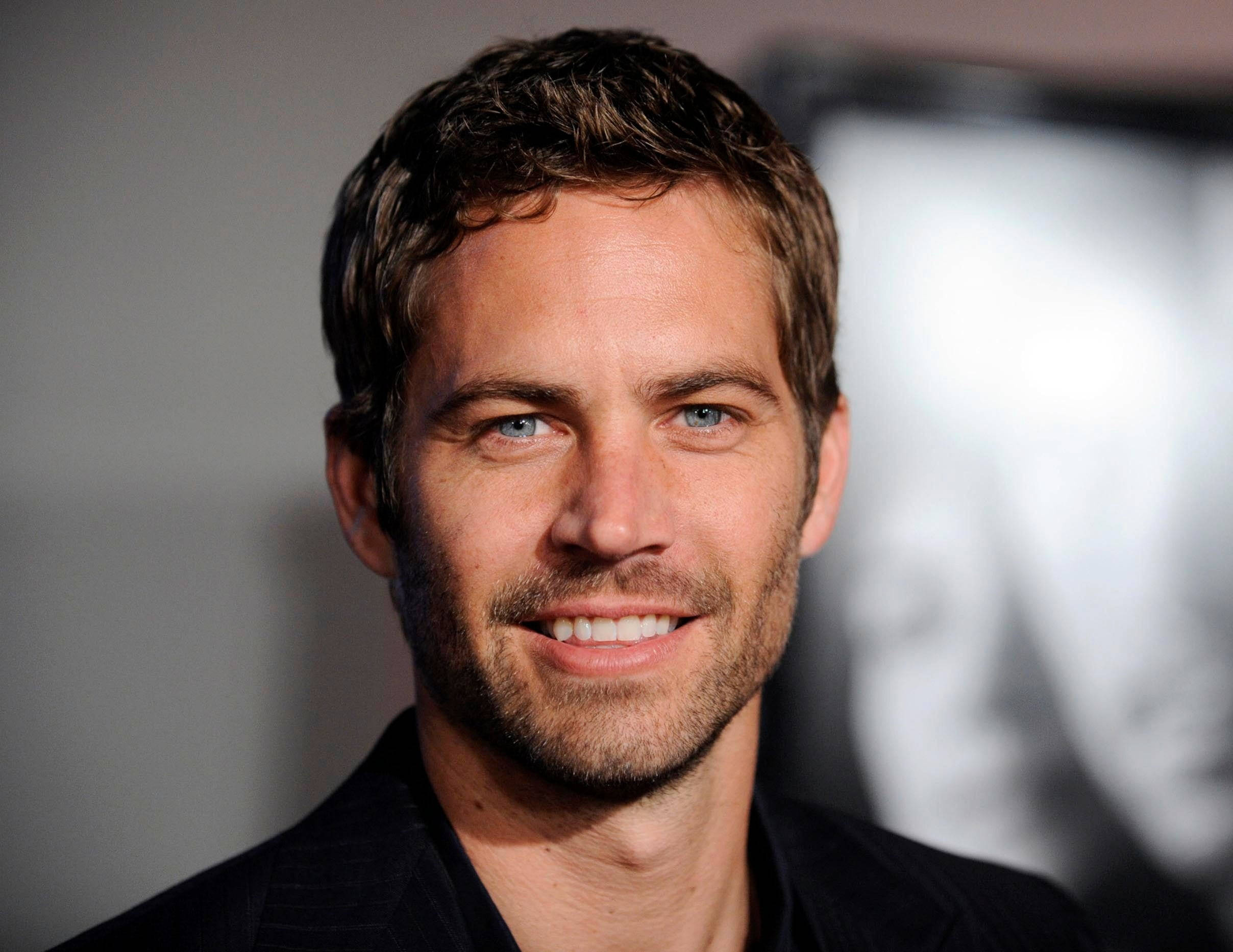 Paul Walker 桌布 壁紙 — 保羅·沃克的特寫肖像，藍眼睛、鬍渣，在模糊背景下溫暖微笑。