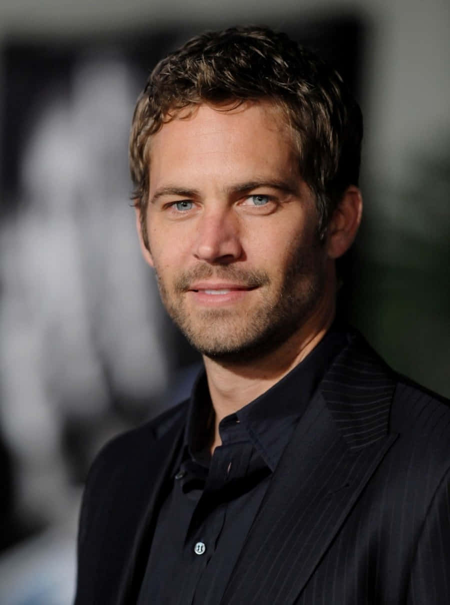Paul Walker 桌布 壁紙 — 保羅·沃克的近距離肖像，身穿深色細條紋西裝，帶著微妙的微笑，背景模糊。