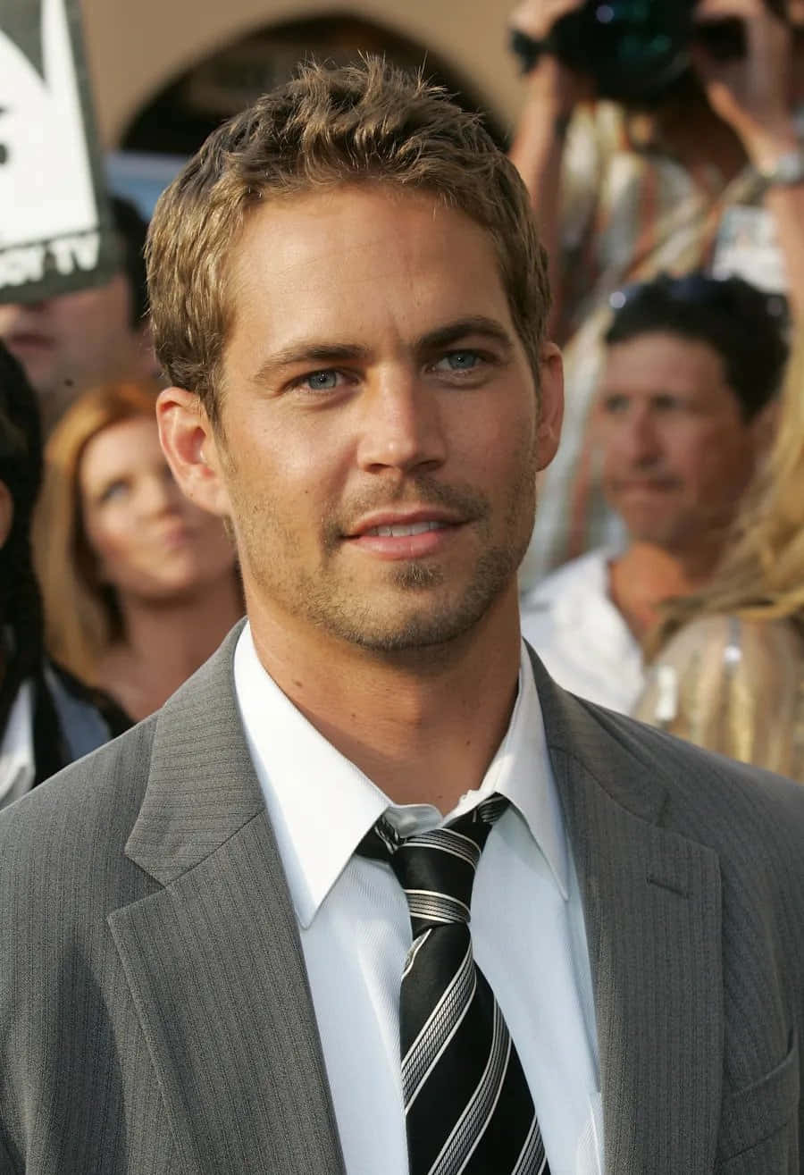 Paul Walker 桌布 壁紙 — 保羅·沃克身穿灰色西裝及條紋領帶，在紅地毯活動上的特寫肖像，身後有模糊的攝影師。