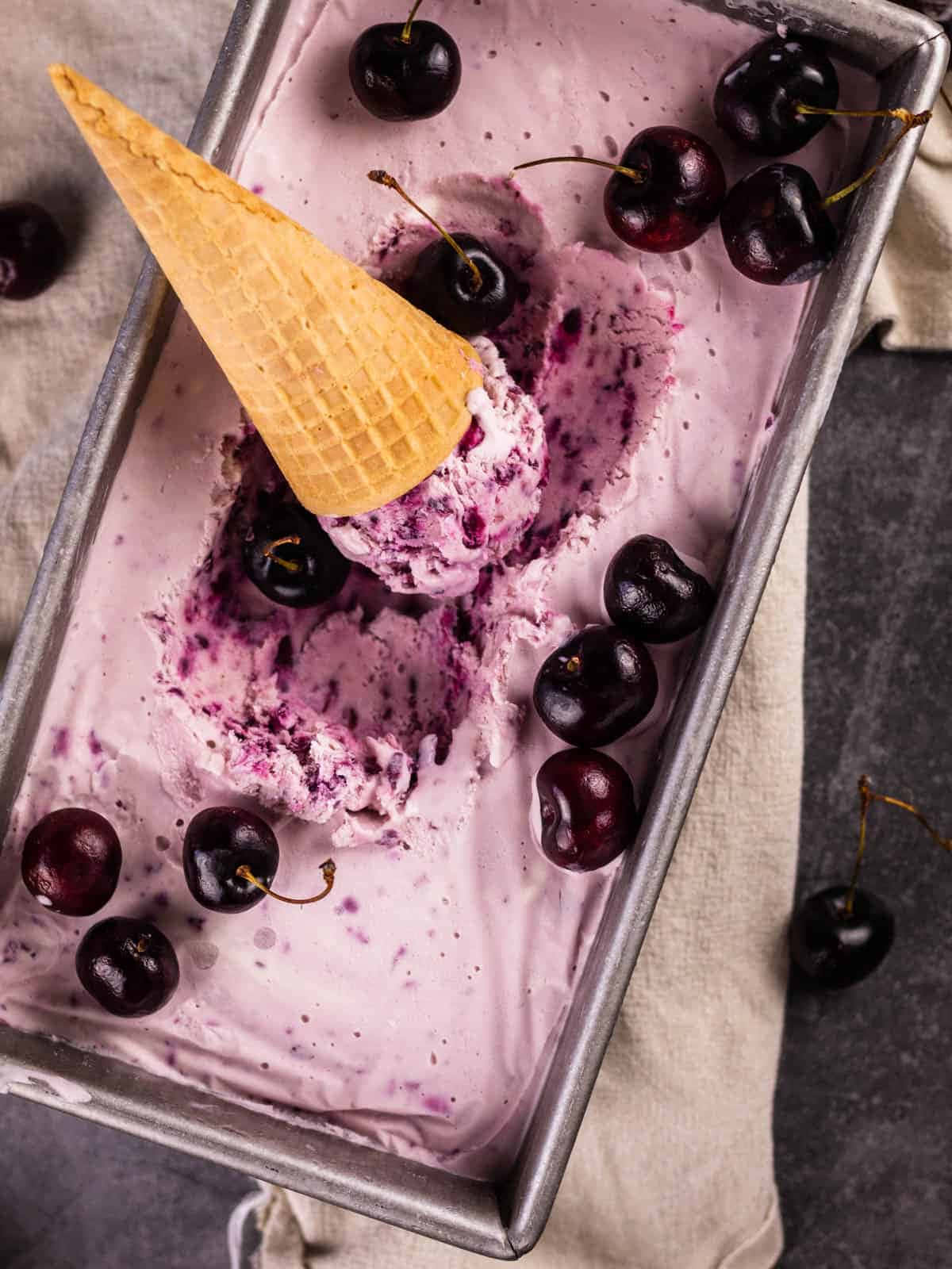 Black Cherry 桌布 壁紙 — 俯拍鏡頭：金屬麵包盤中的紫色櫻桃冰淇淋，上面鋪滿新鮮櫻桃和一個鬆餅筒冰淇淋球。