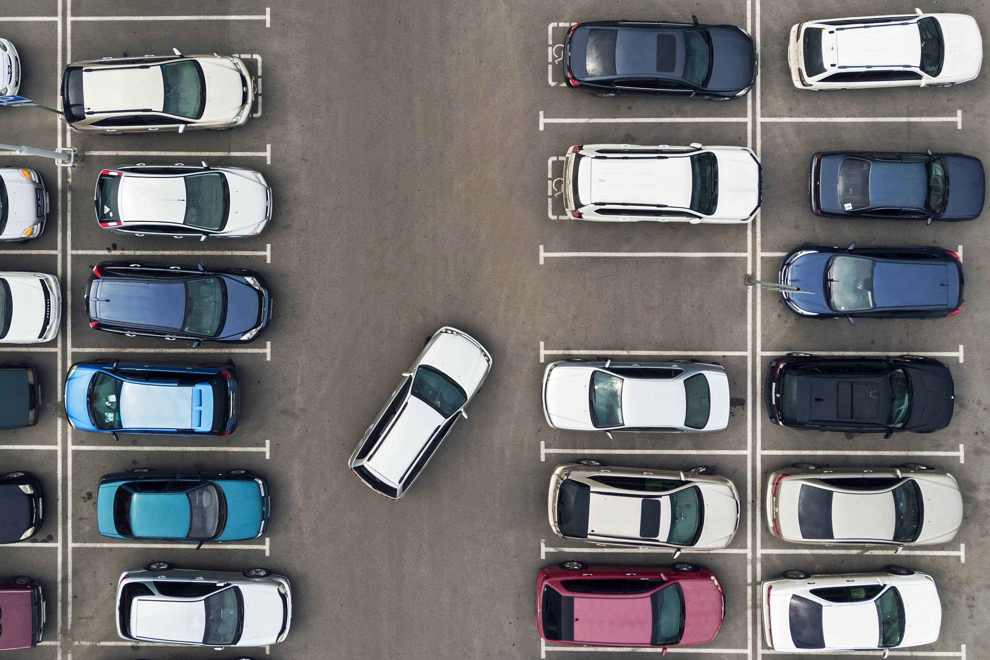 汽車 桌布 壁紙 — 俯瞰一個停車場，裡面停滿了色彩繽紛的汽車，整齊地排列成行，中間有一輛白色汽車斜停。