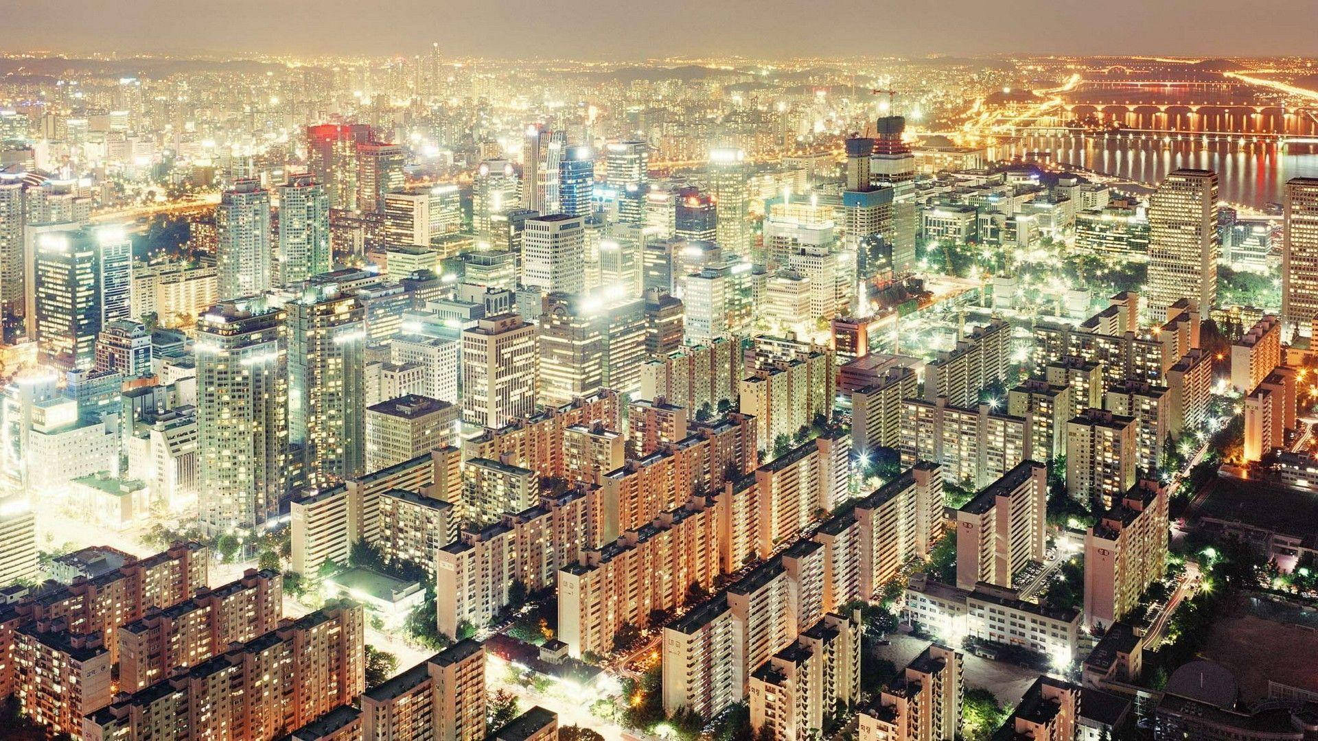南韓 桌布 壁紙 — 俯瞰一個在夜間蔓延的城市，閃爍的摩天大樓和住宅區被溫暖的人造燈光照亮。